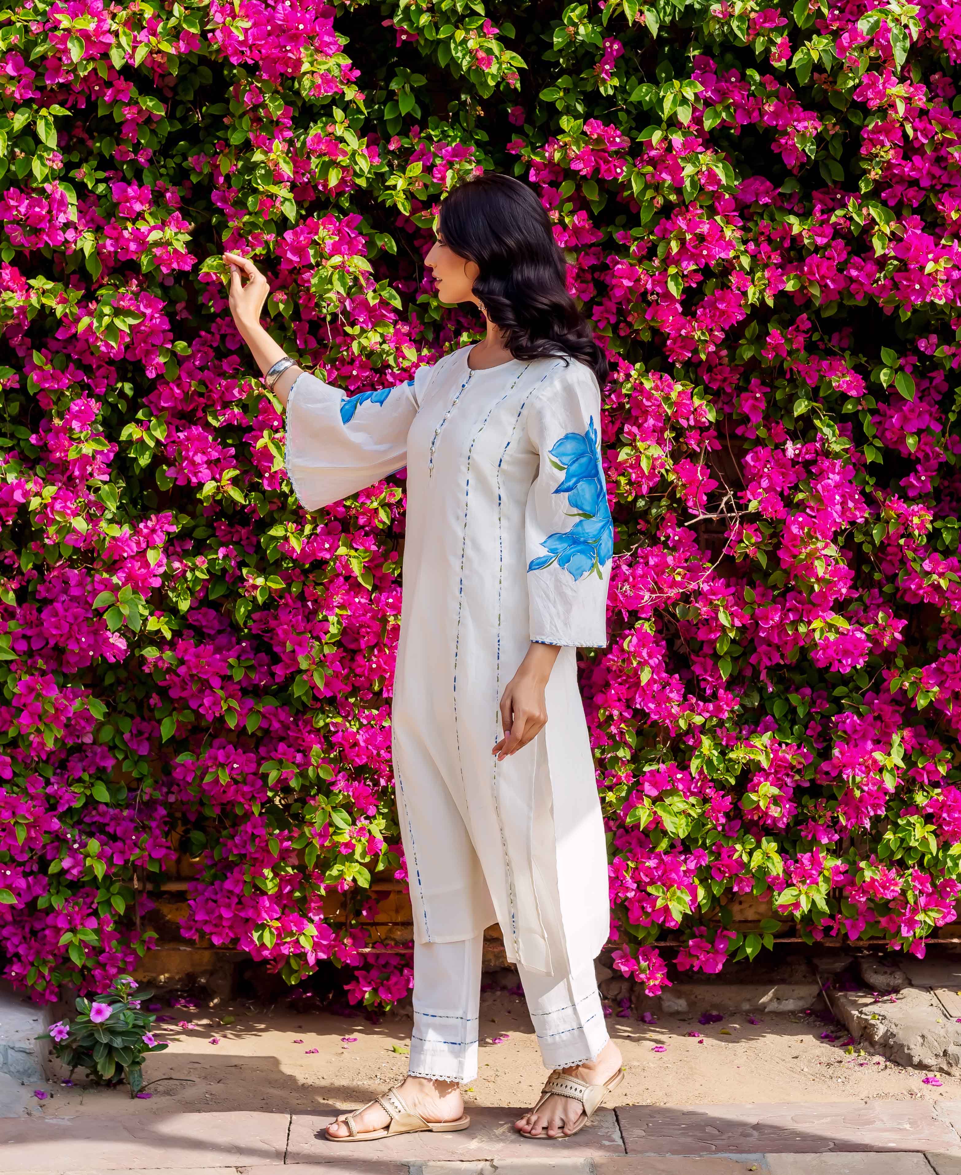 Side angle of model wearing cream kurta and pants with blue brush-painted floral sleeves.