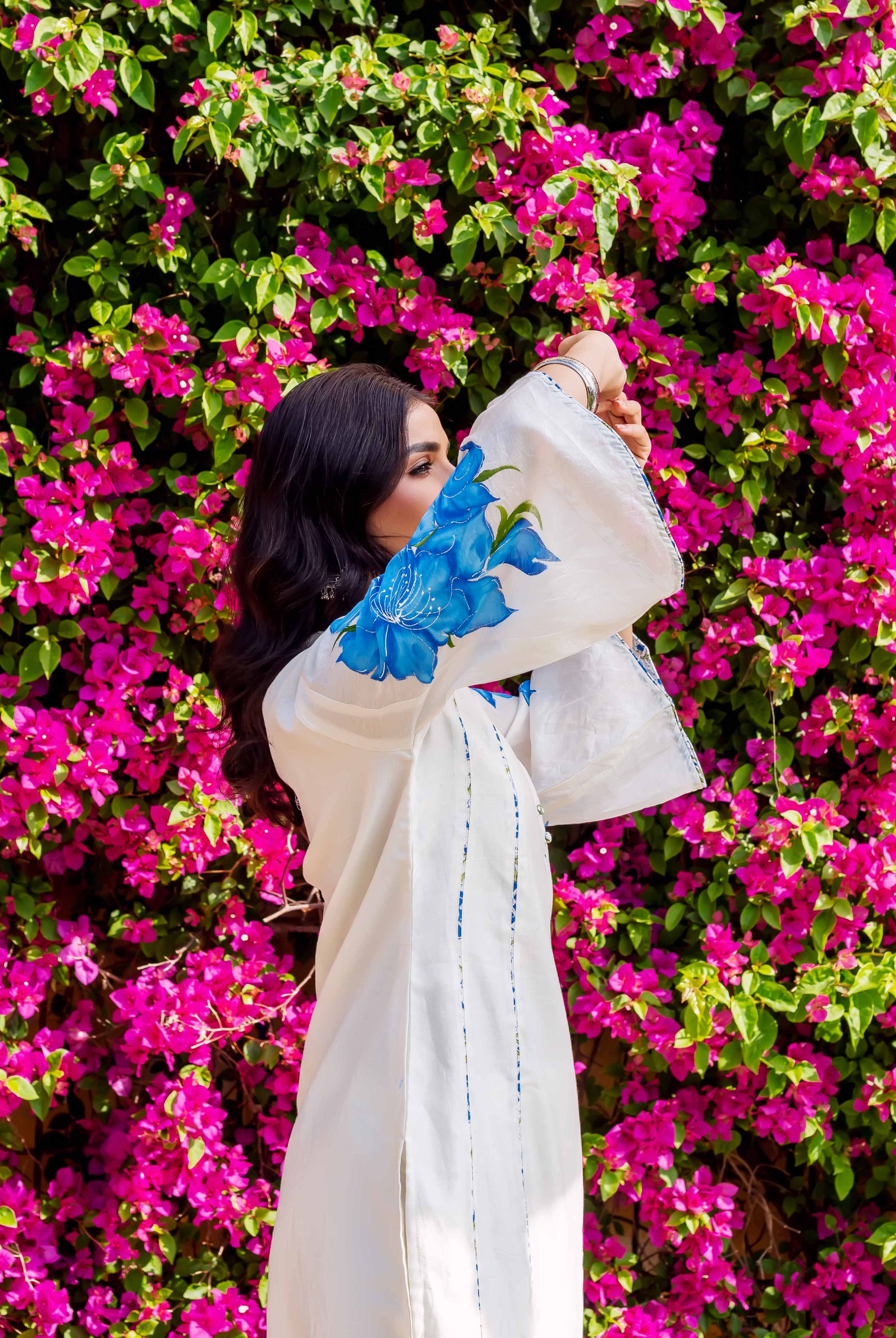 Side view model in white kurta with blue brush-painted floral sleeve, pink flower background.