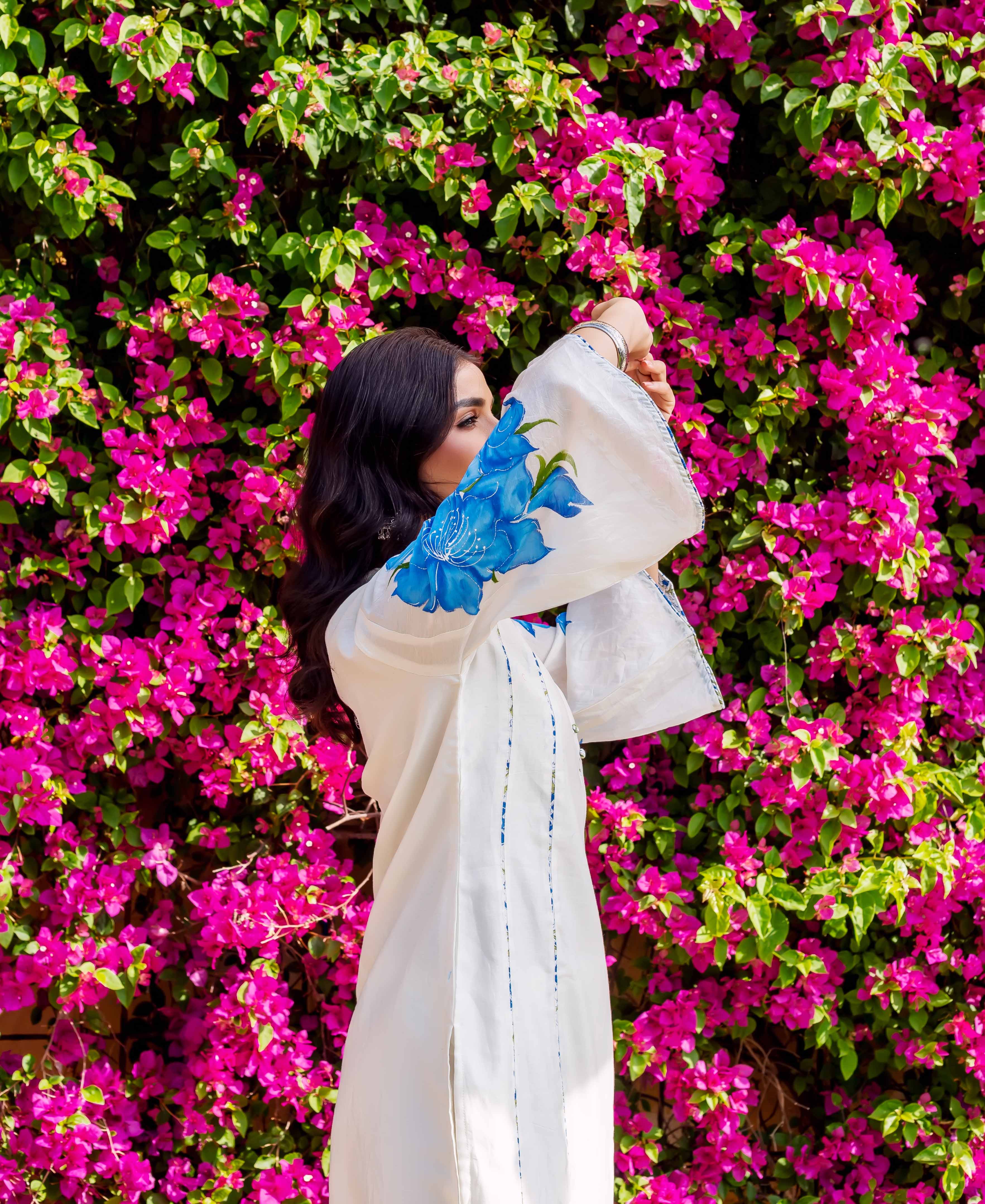 Side view model in white kurta with blue brush-painted floral sleeve, pink flower background.