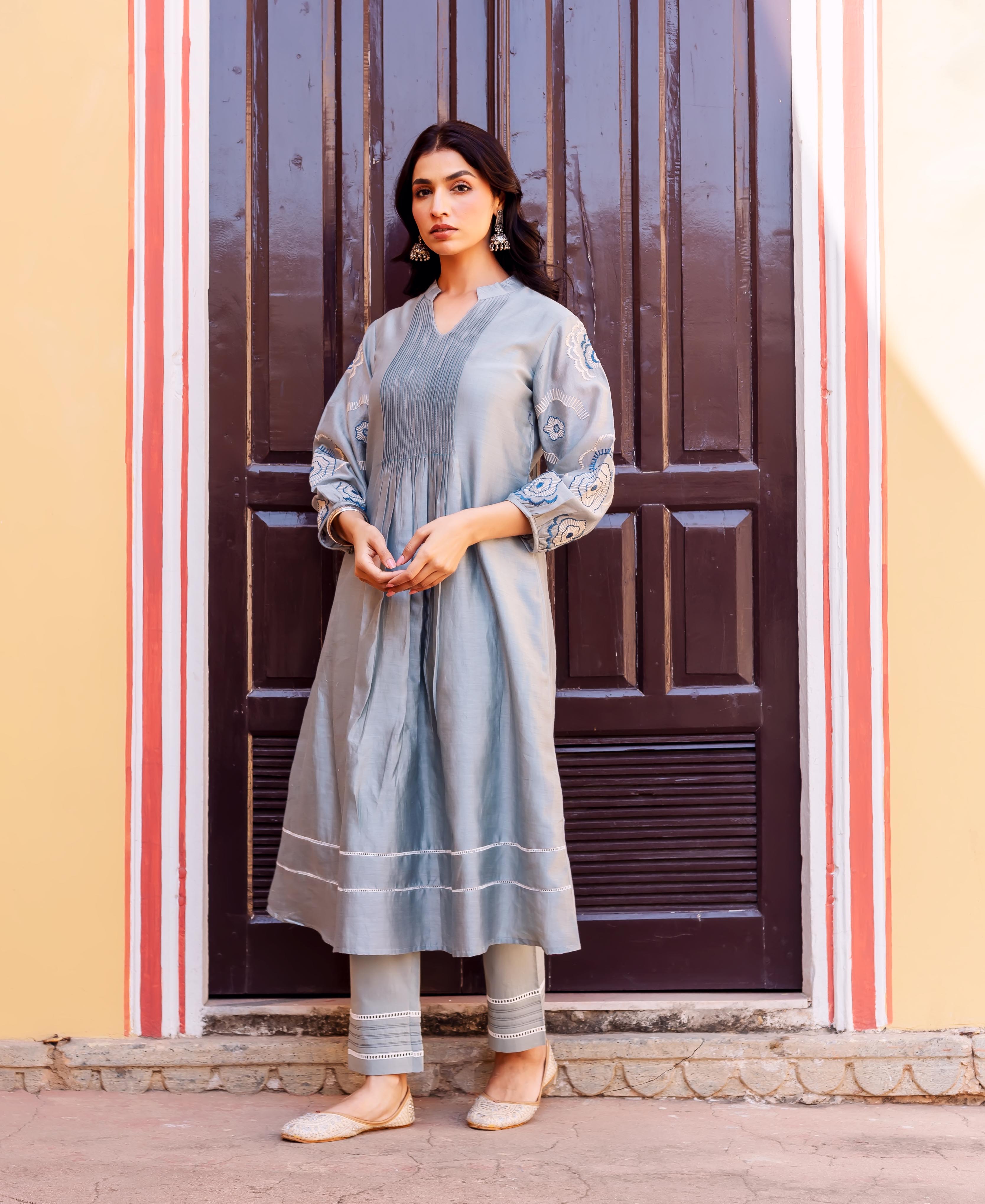 Woman in a slate blue kurta set featuring pintucks and ethnic patterns on sleeves.