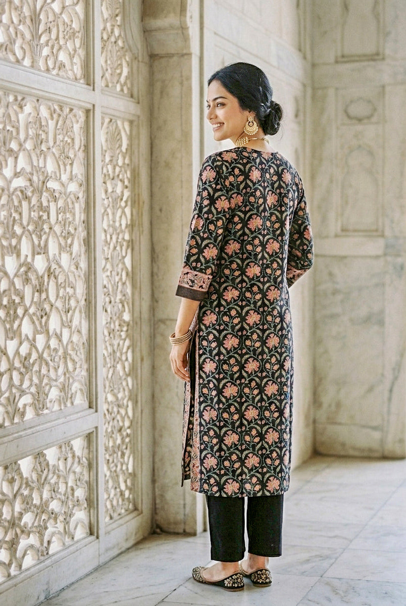 Side view of model wearing black floral hand block printed kurta and black pants.