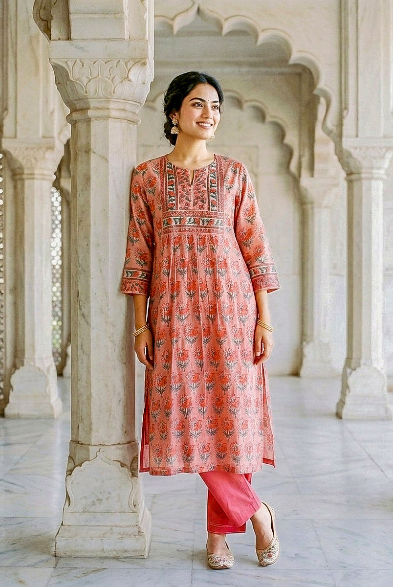 Smiling model wears coral hand block print floral kurta with matching pants, full front view.