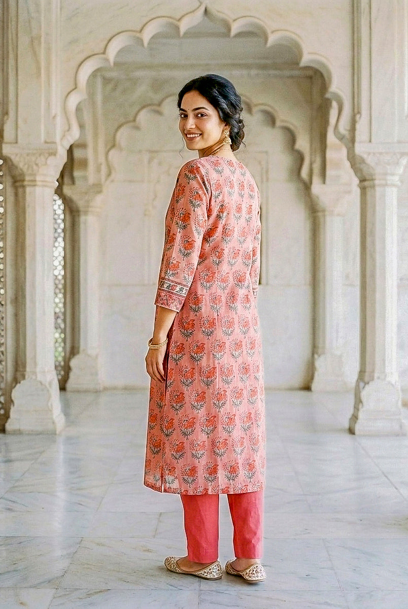 Side-back view of model in coral hand block print kurta with floral motifs and coral pants.