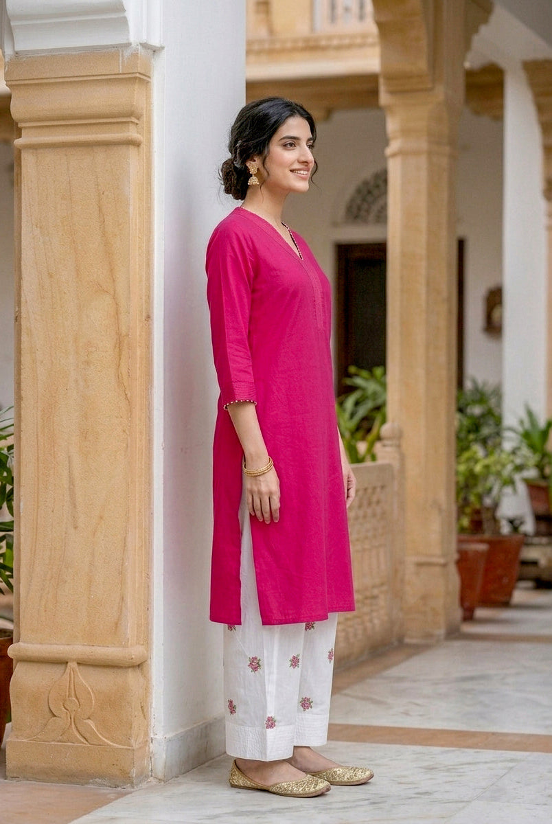 Side view of smiling model wearing fuchsia pink cotton kurta and white embroidered salwar.