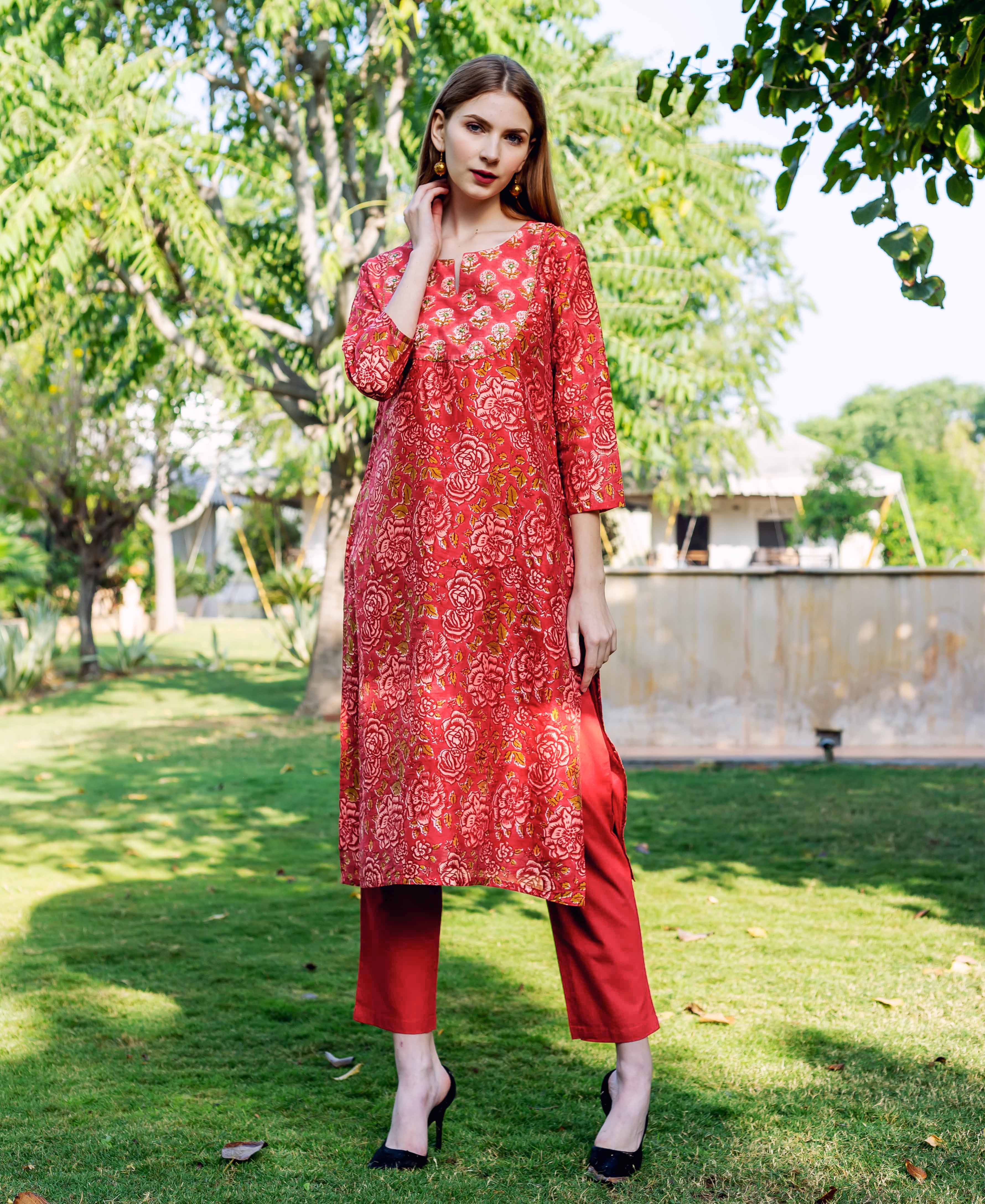 Woman models a red hand-block printed floral kurta and matching pants, standing outside.