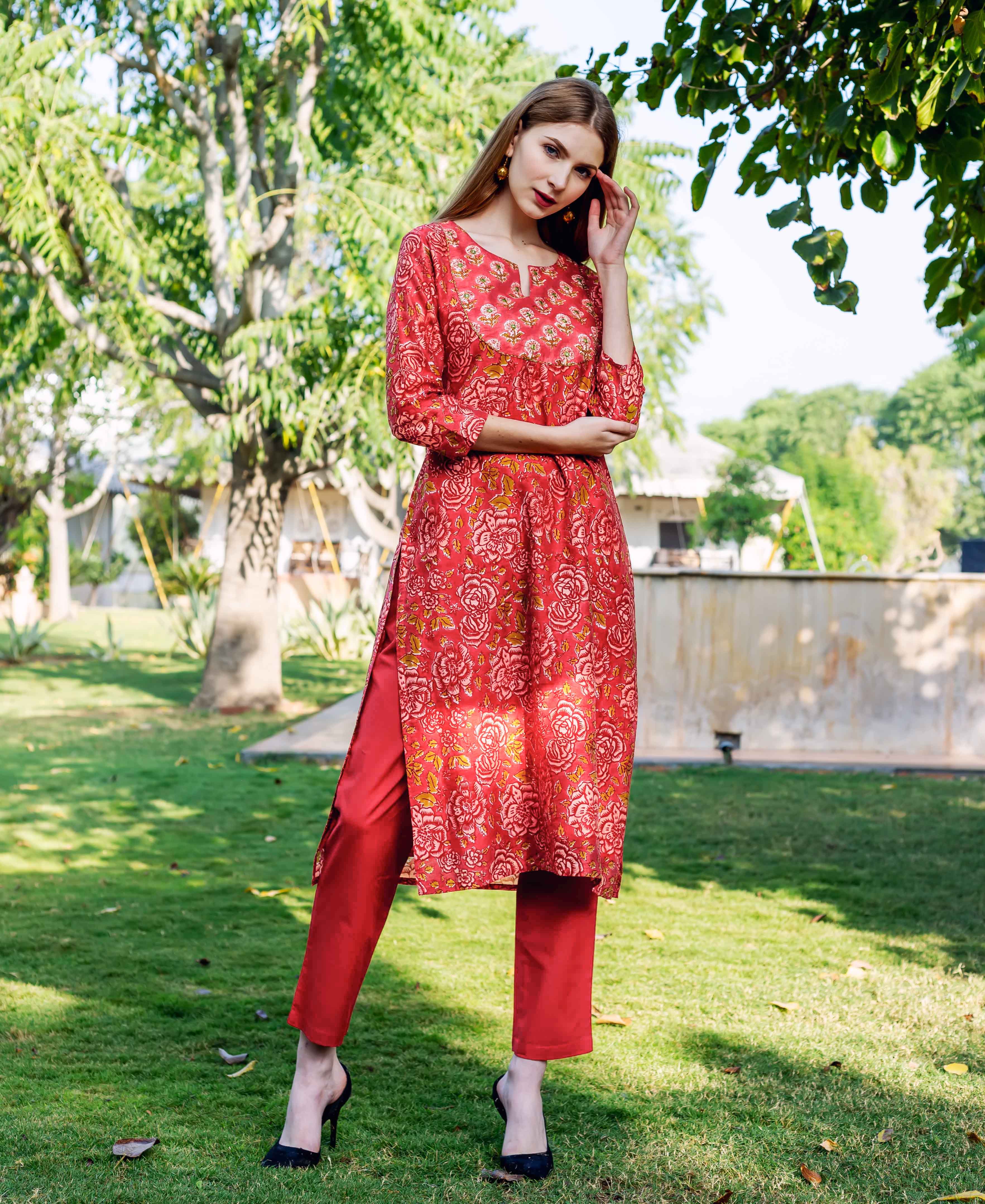 Model wearing a red floral hand-block printed kurta set, standing on green grass.