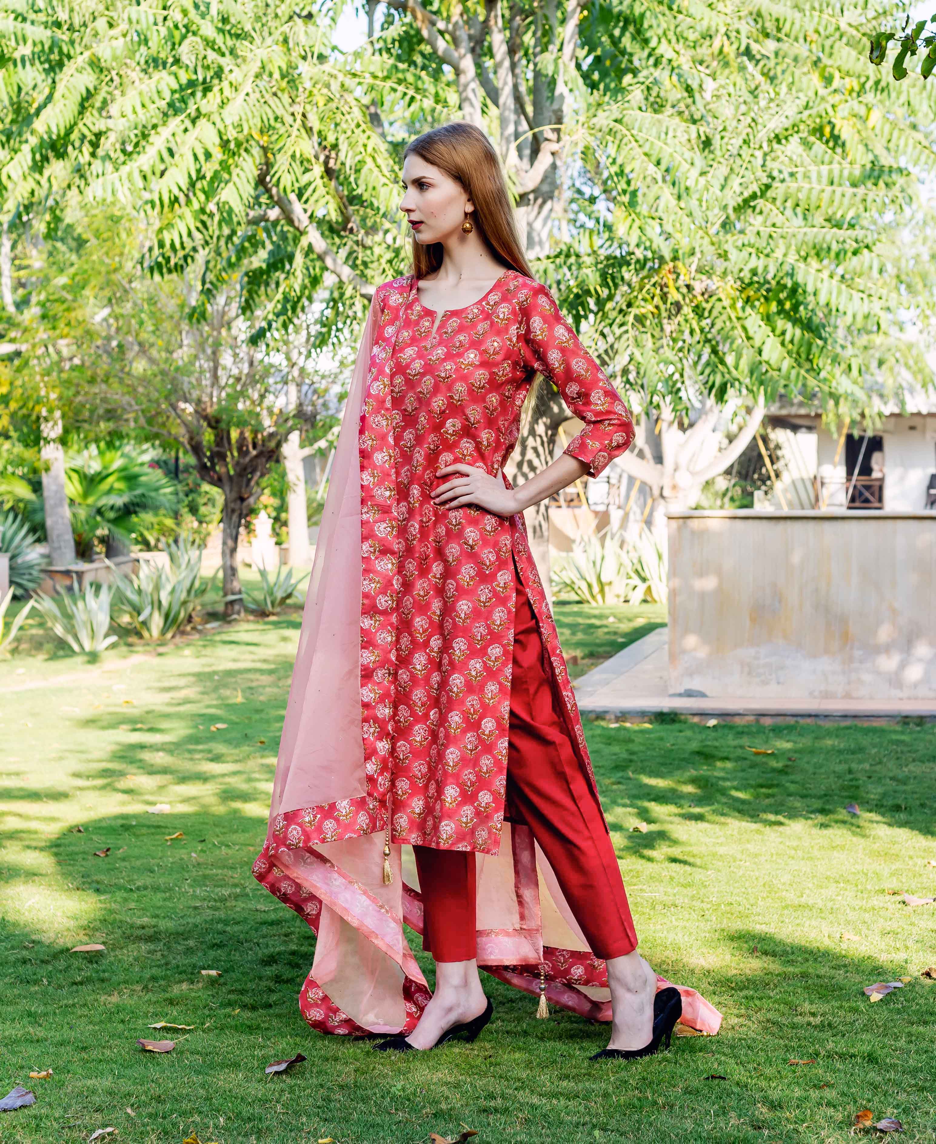 Model wearing a red floral hand-block printed straight kurta set with sheer pink dupatta outdoors.