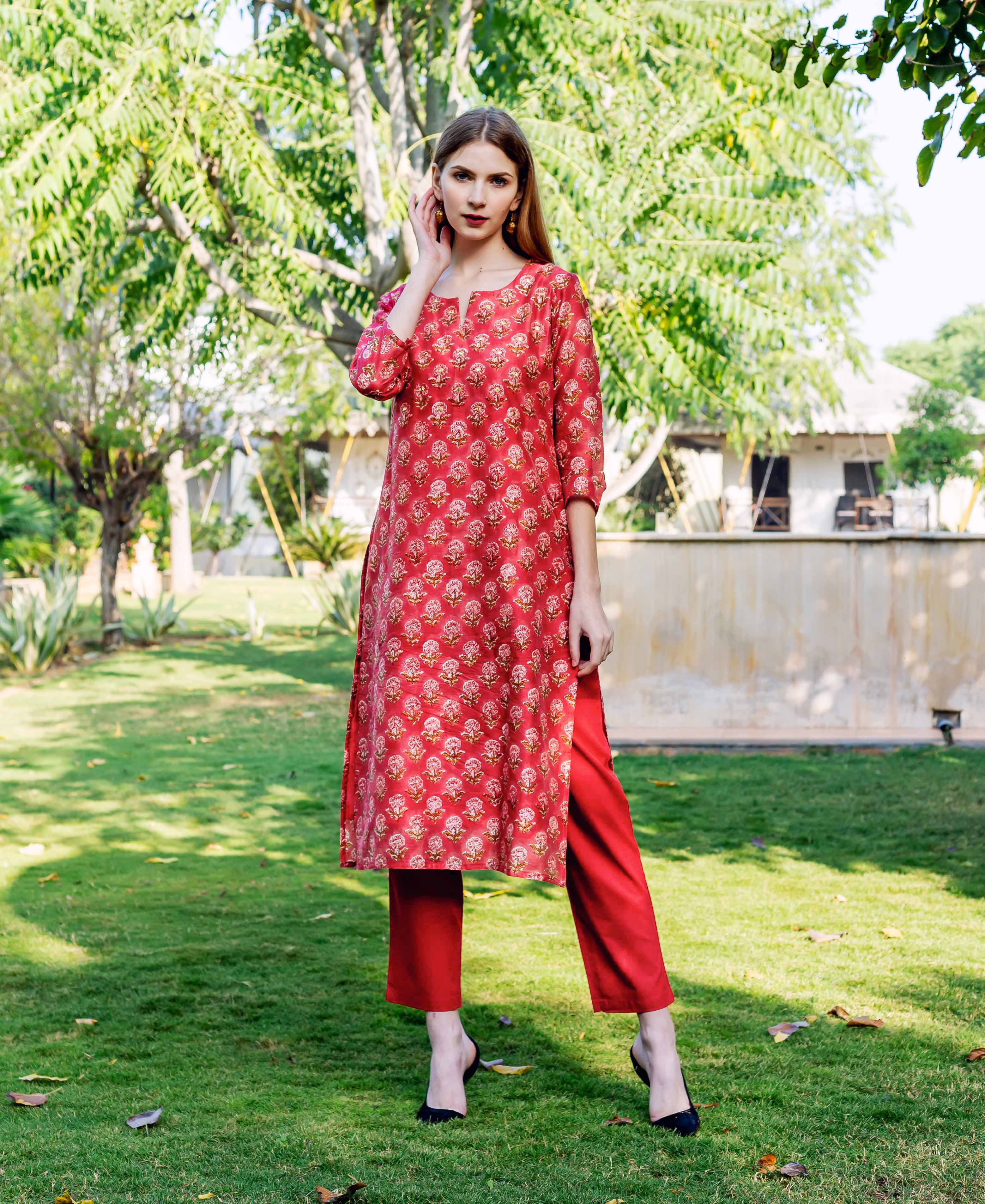 Woman in a red straight kurta with small floral print and matching trousers, standing outdoors.