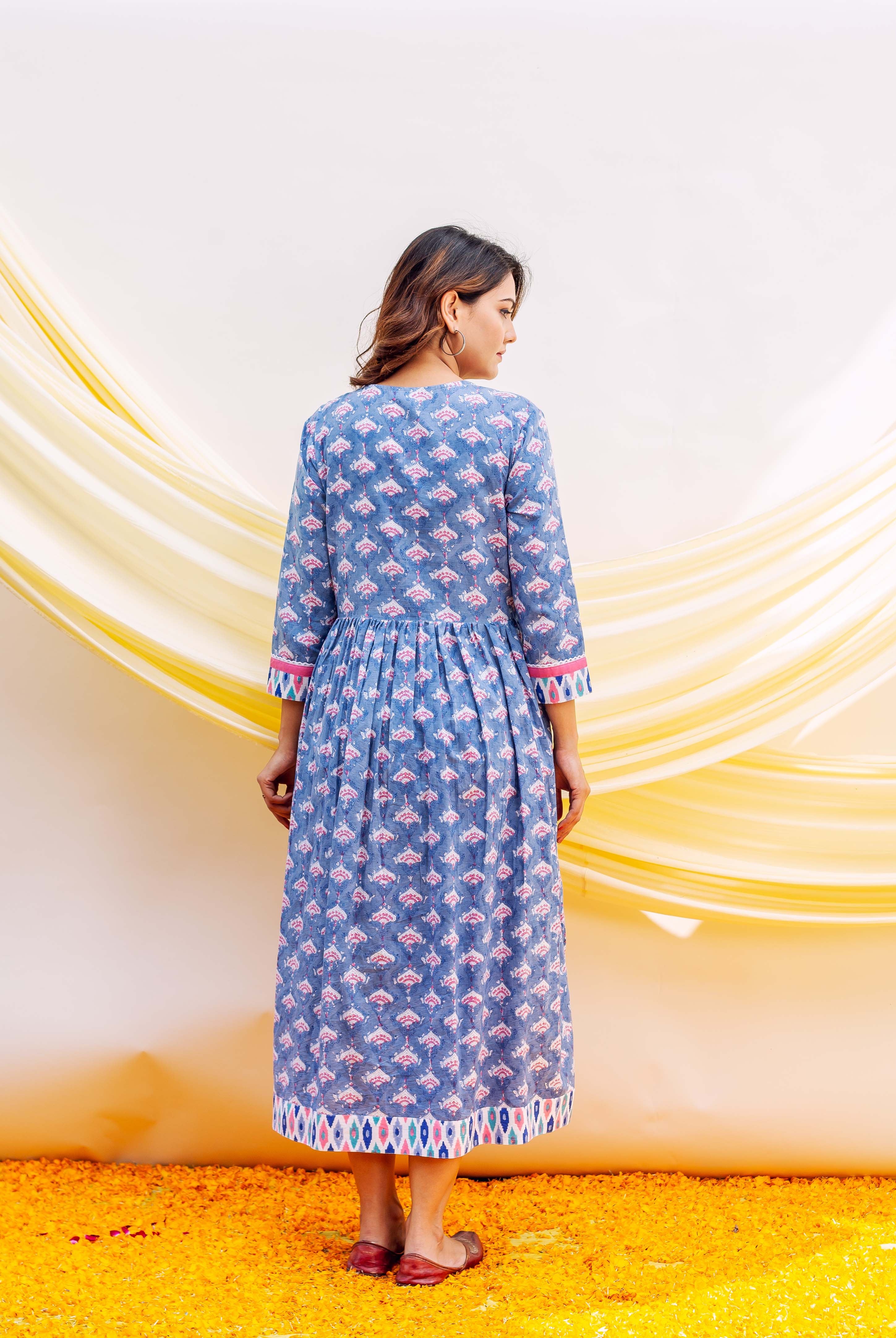 Back view of model in blue block-printed cotton midi dress with pink ethnic motifs and gathered waist.