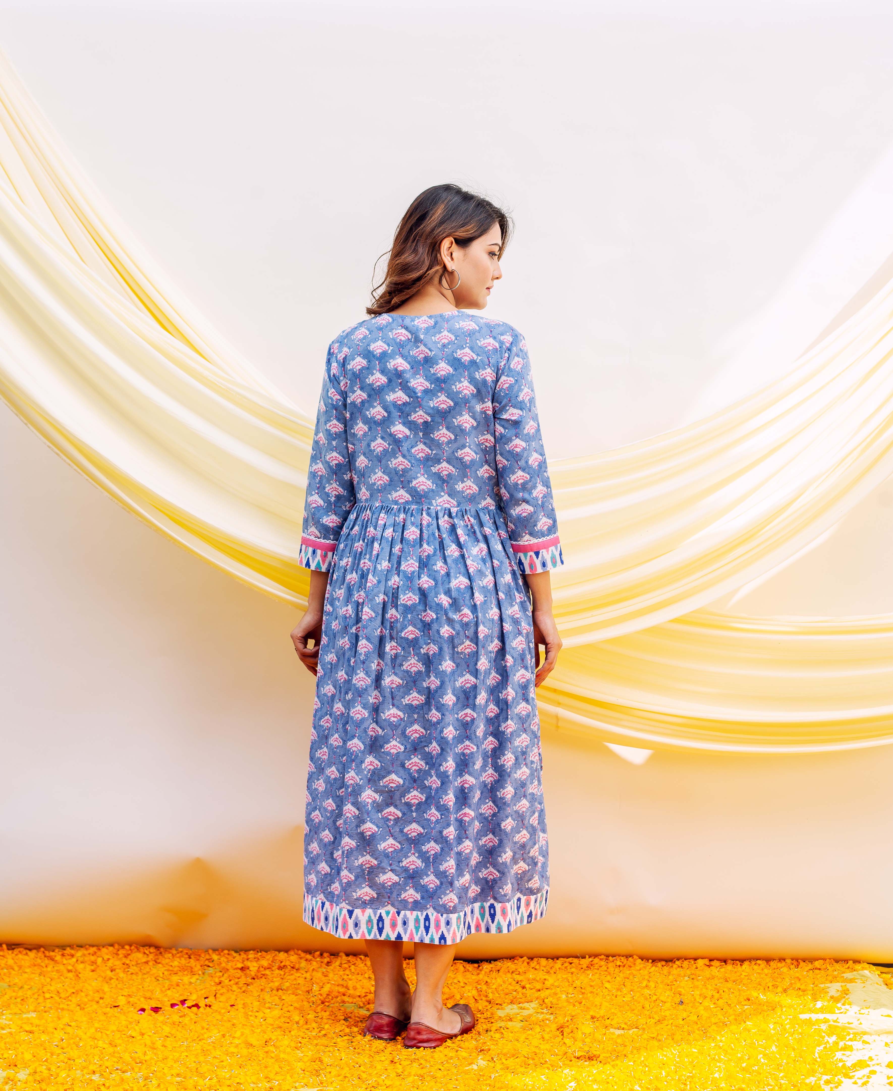Back view of model in blue block-printed cotton midi dress with pink ethnic motifs and gathered waist.