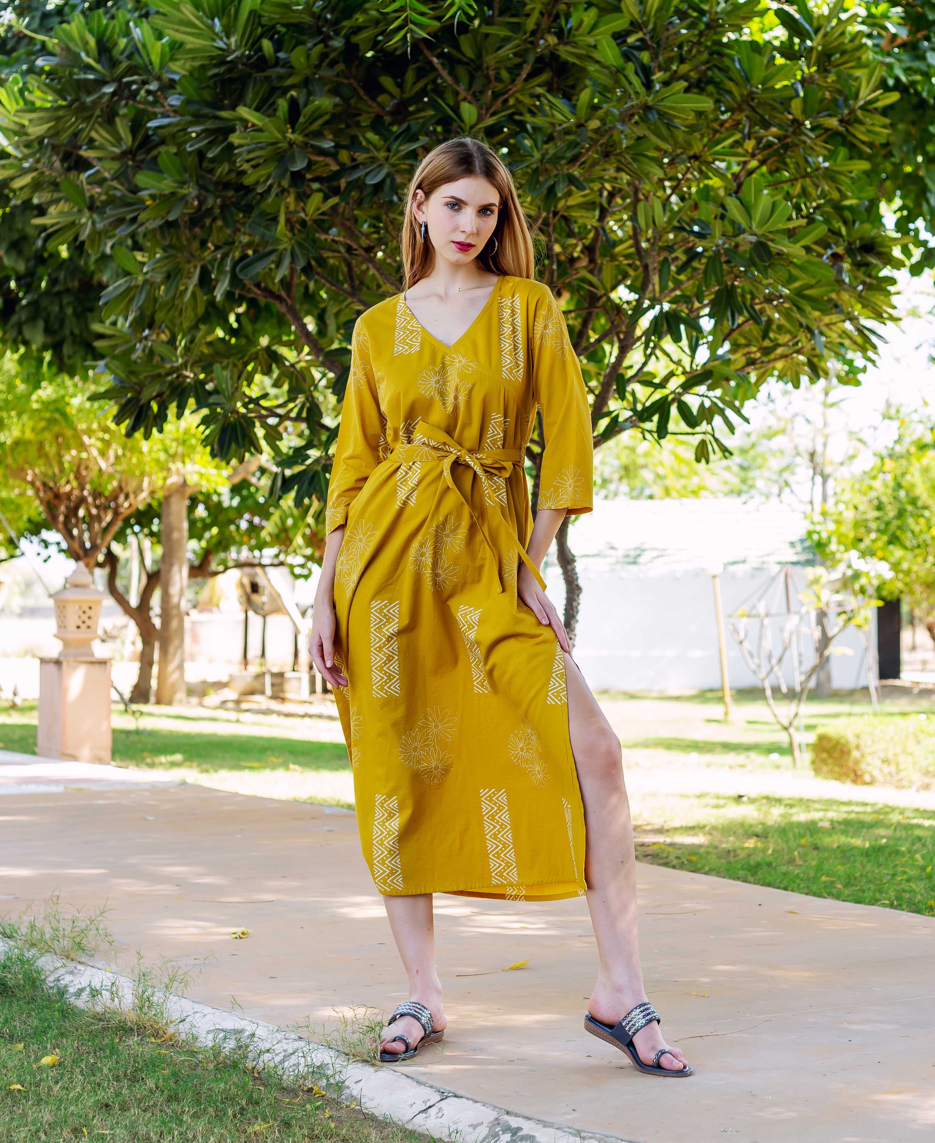 A model wearing a yellow dress with white block print, standing outdoors.