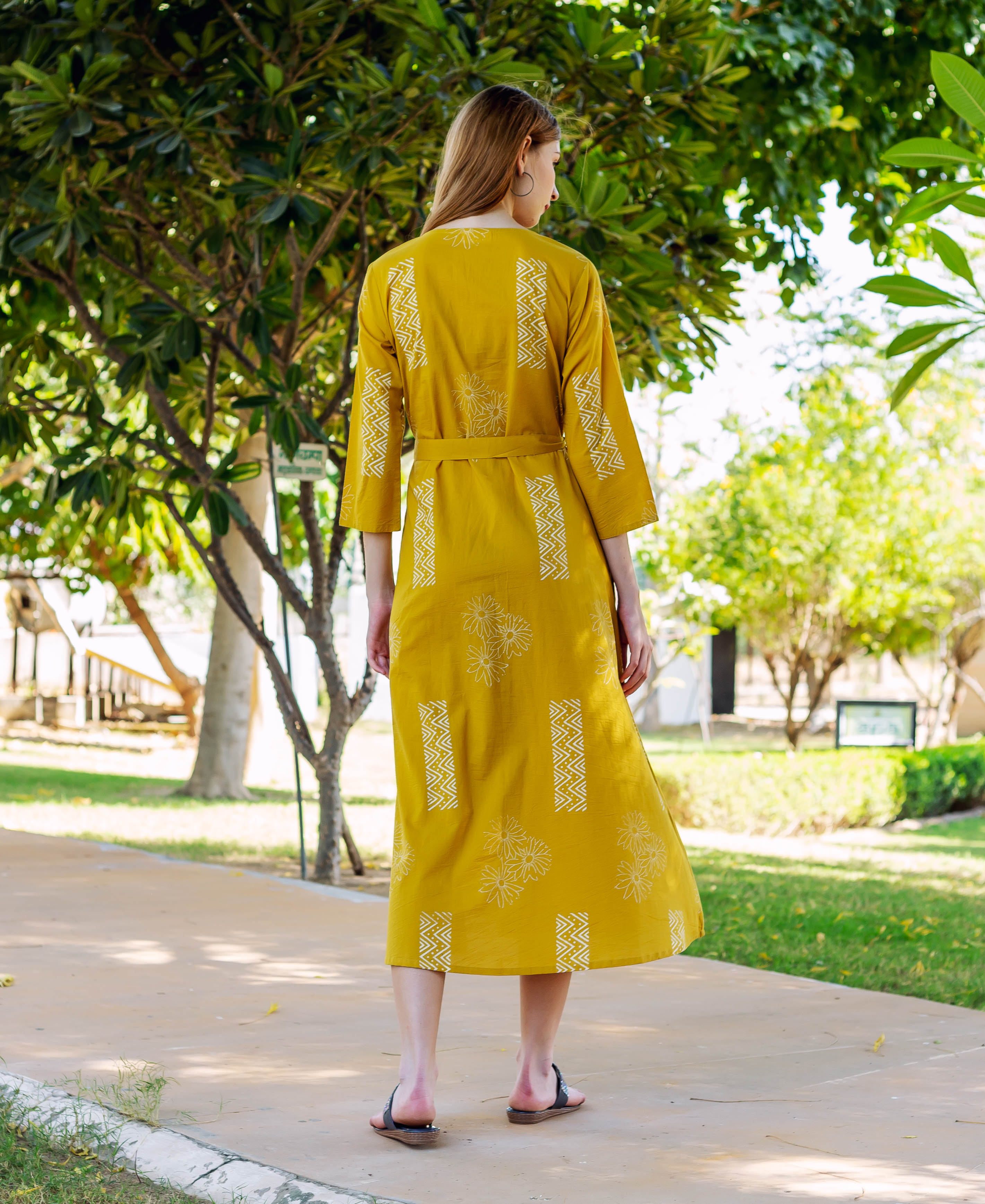 Rear view of model in belted mustard yellow hand-block-printed dress with white patterns.