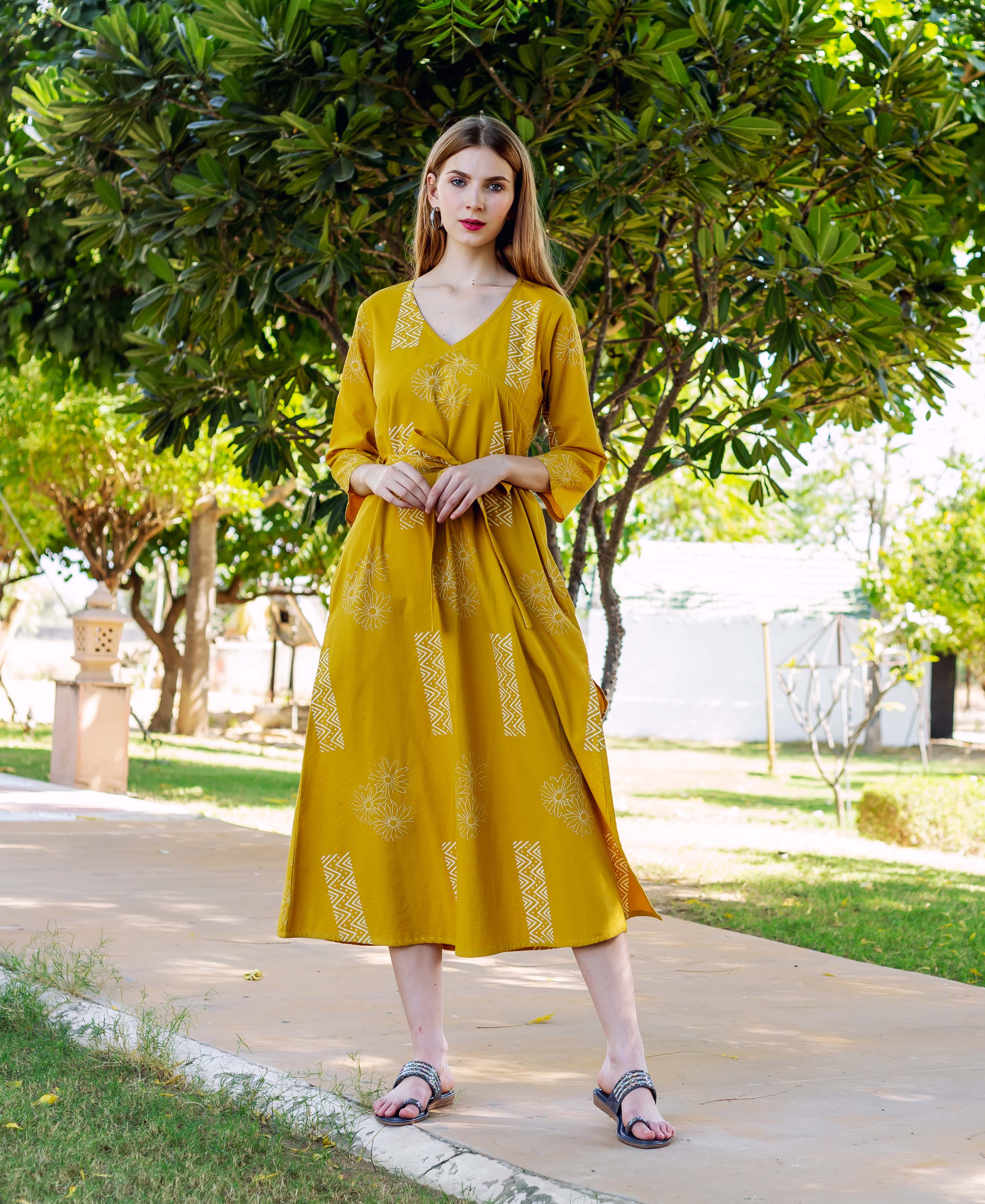 A model wearing a yellow dress with white block prints, standing outdoors.