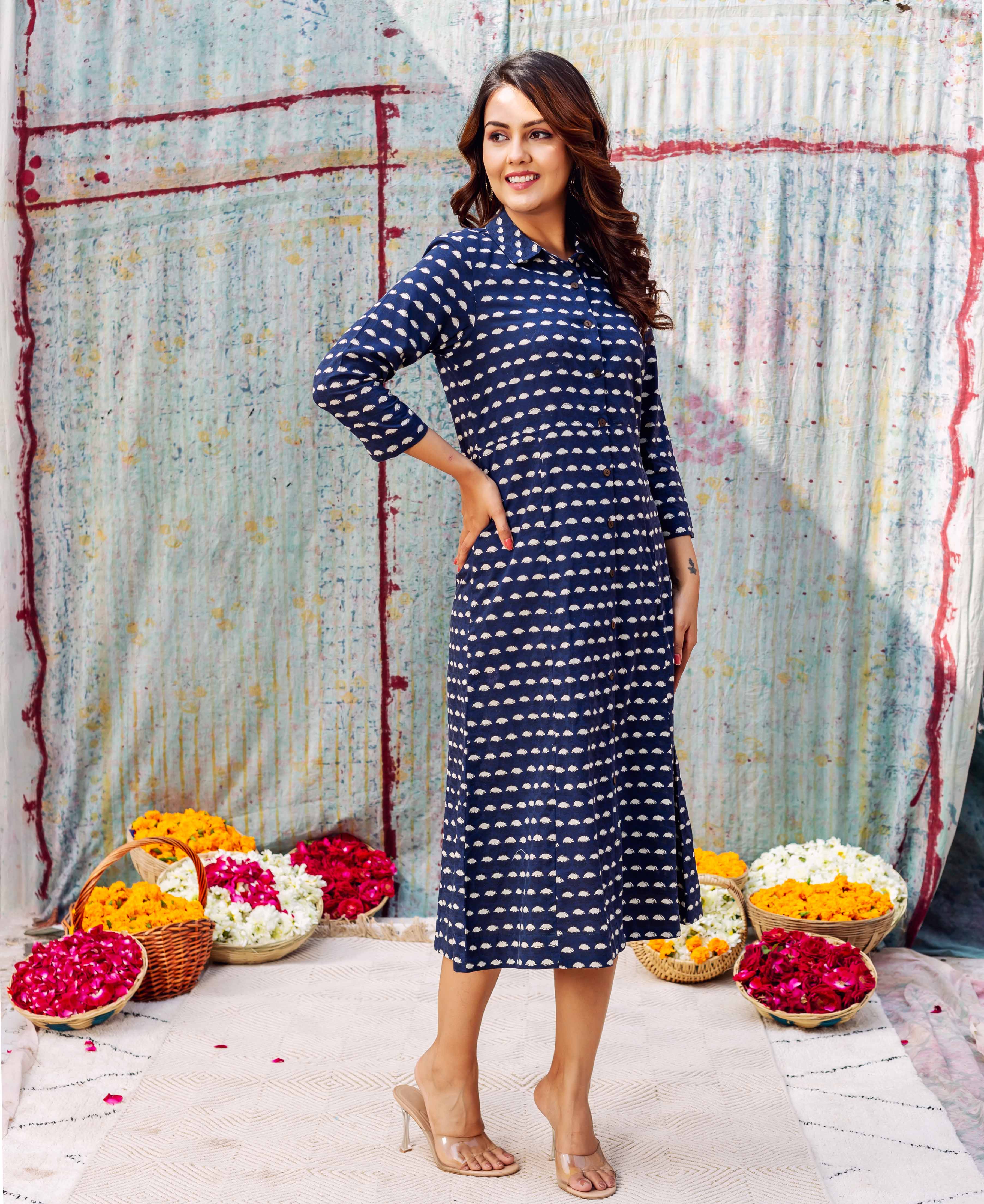 Woman in dark blue dress with white leaf-like pattern, posing with hand on hip.