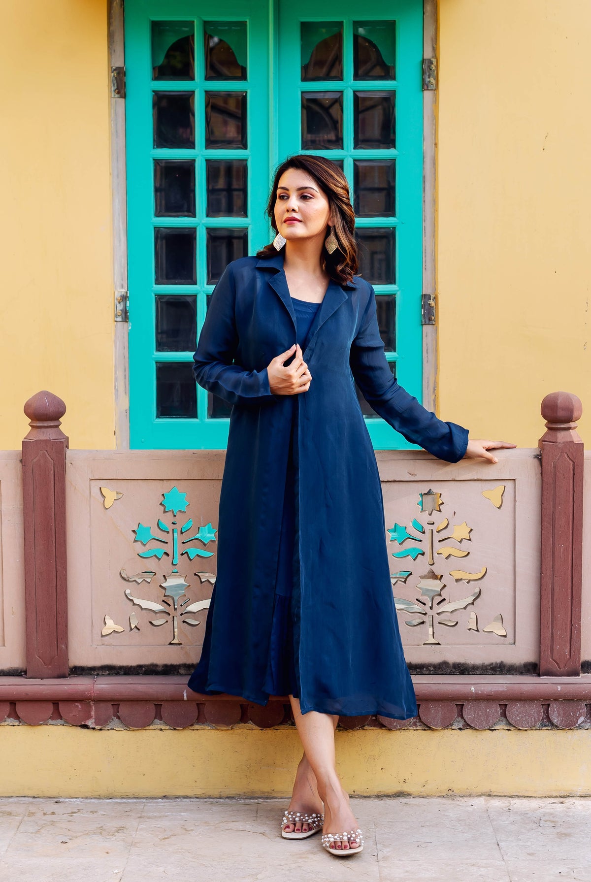 Model stands in a twilight blue long jacket and dress, paired with pearl sandals.