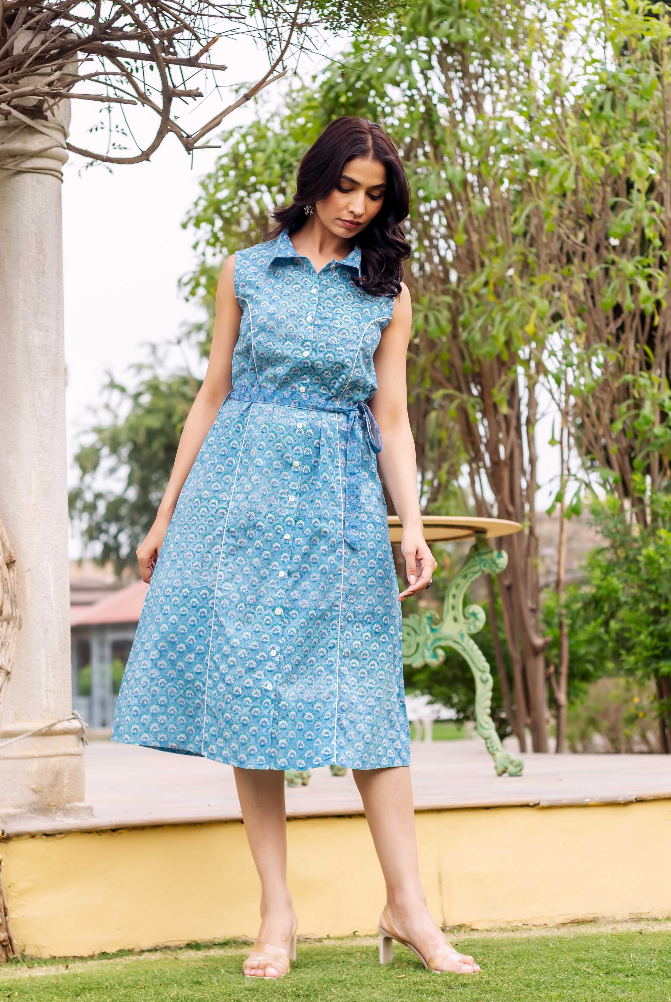 Model wears a blue sleeveless collared button-down dress with an intricate light blue print.