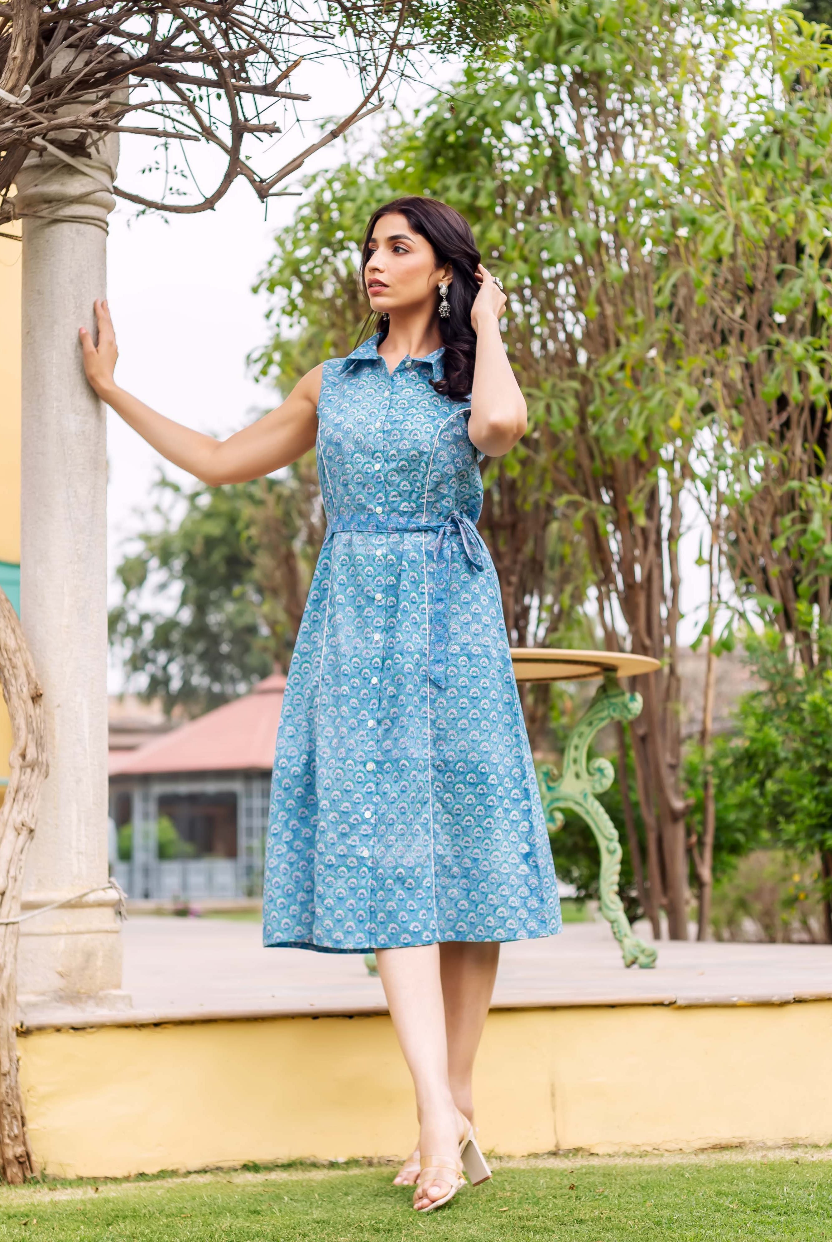 Model in blue sleeveless collared button-down dress with ethnic block print and belted waist.