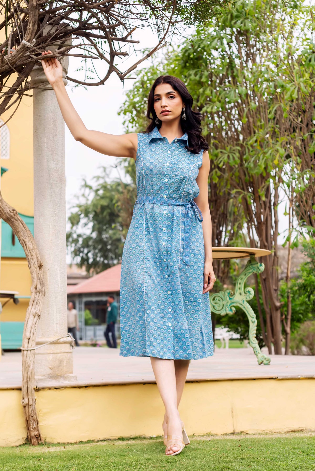 Full-length model in a blue hand-block-printed sleeveless button-down dress with a tie-belt.