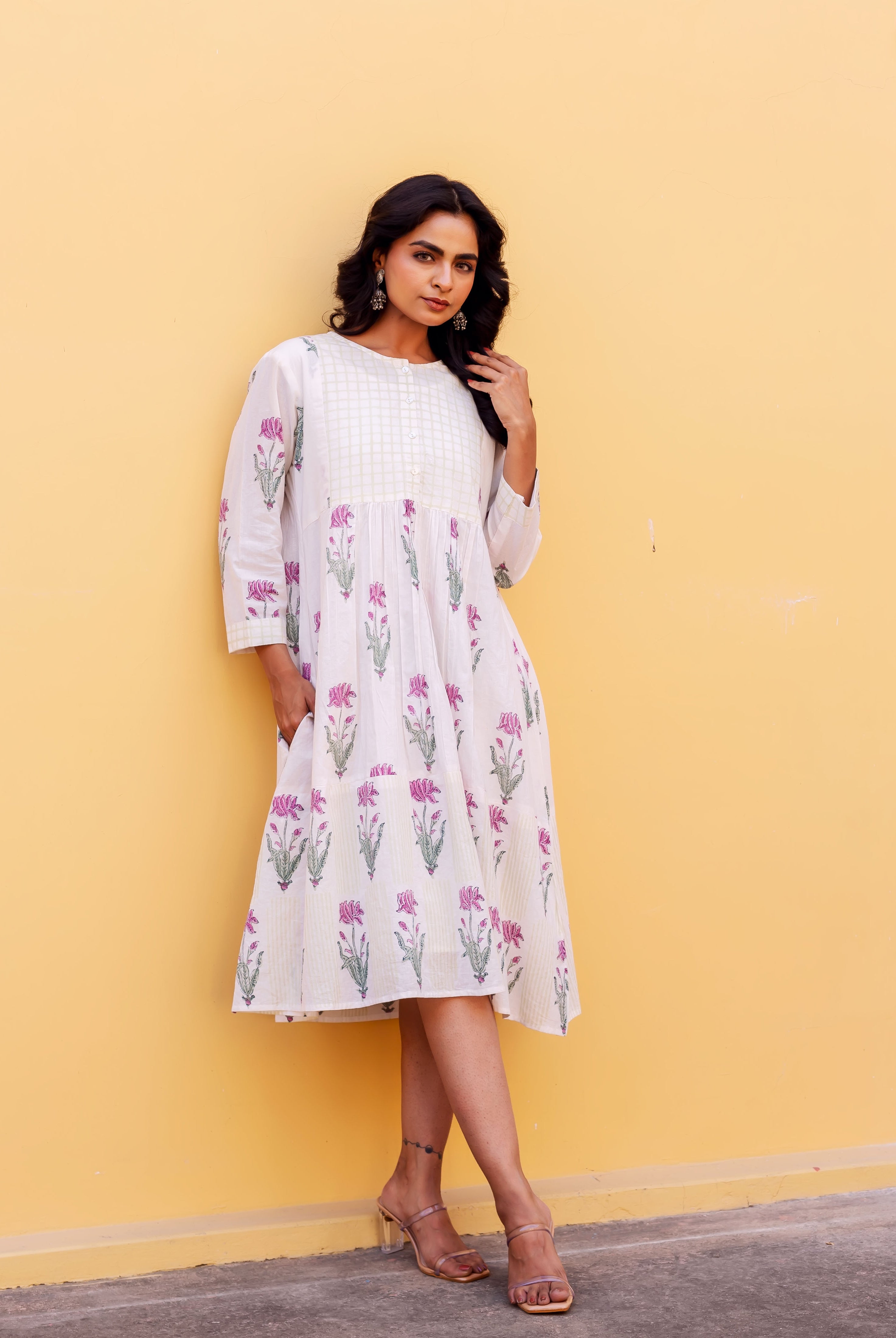 Model wears a white block-printed cotton dress with pink floral print and side pockets.