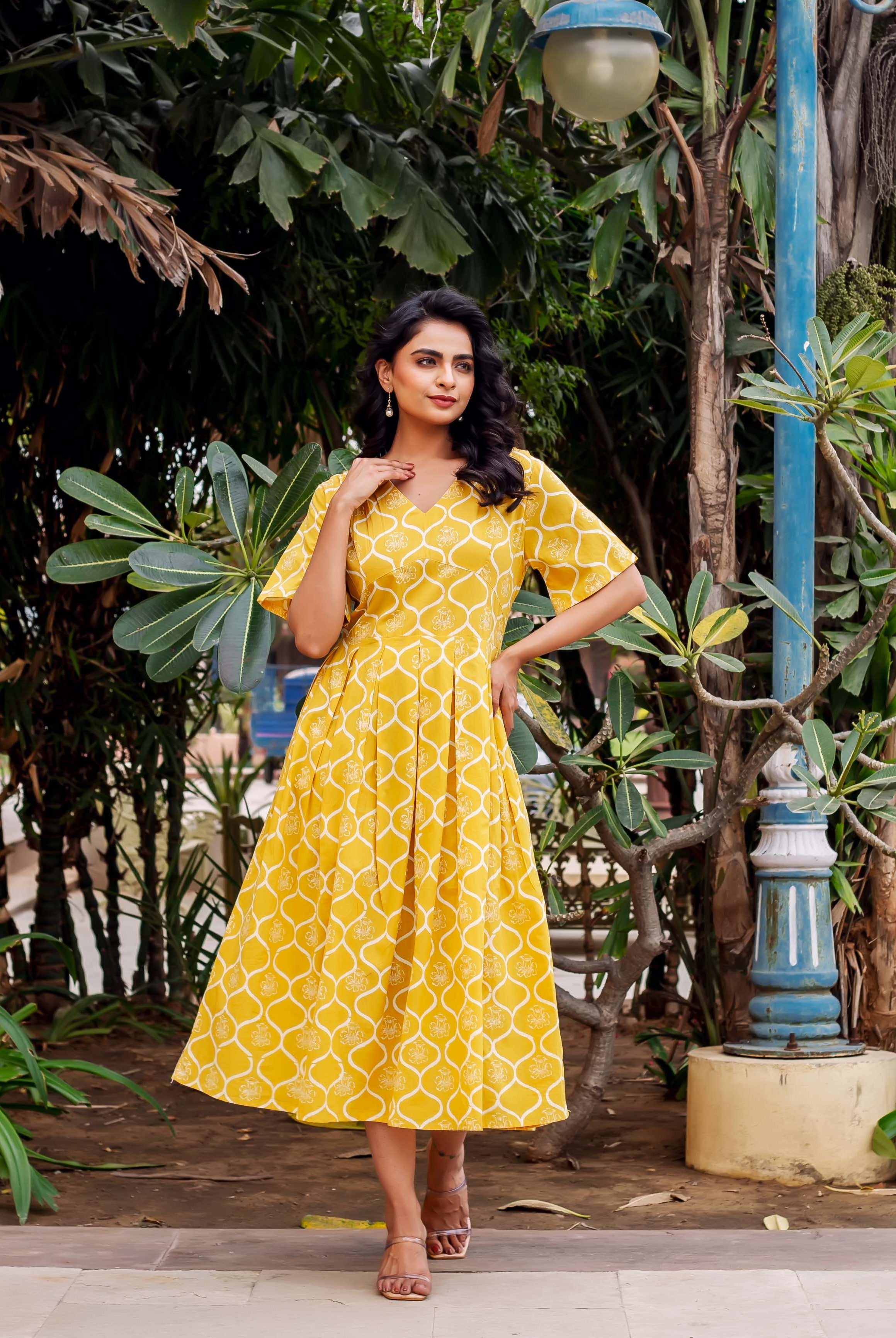 Woman in a radiant mustard yellow V-neck midi dress with white geometric block print.