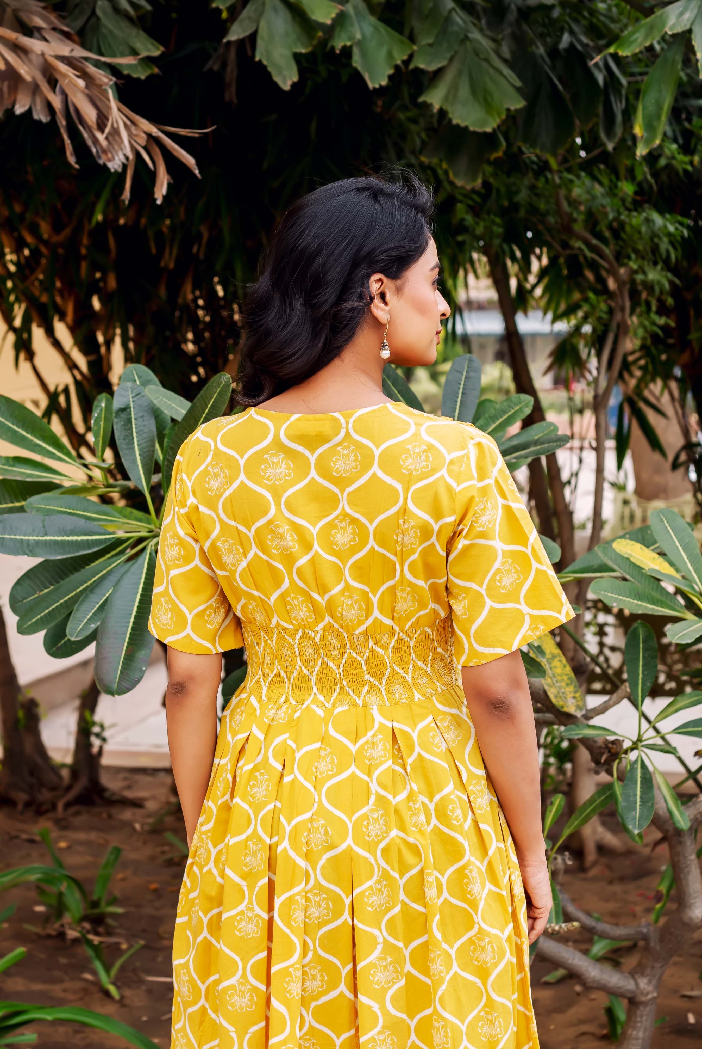 Back view of woman in mustard yellow hand-block printed dress with shirred waist, pleated skirt.