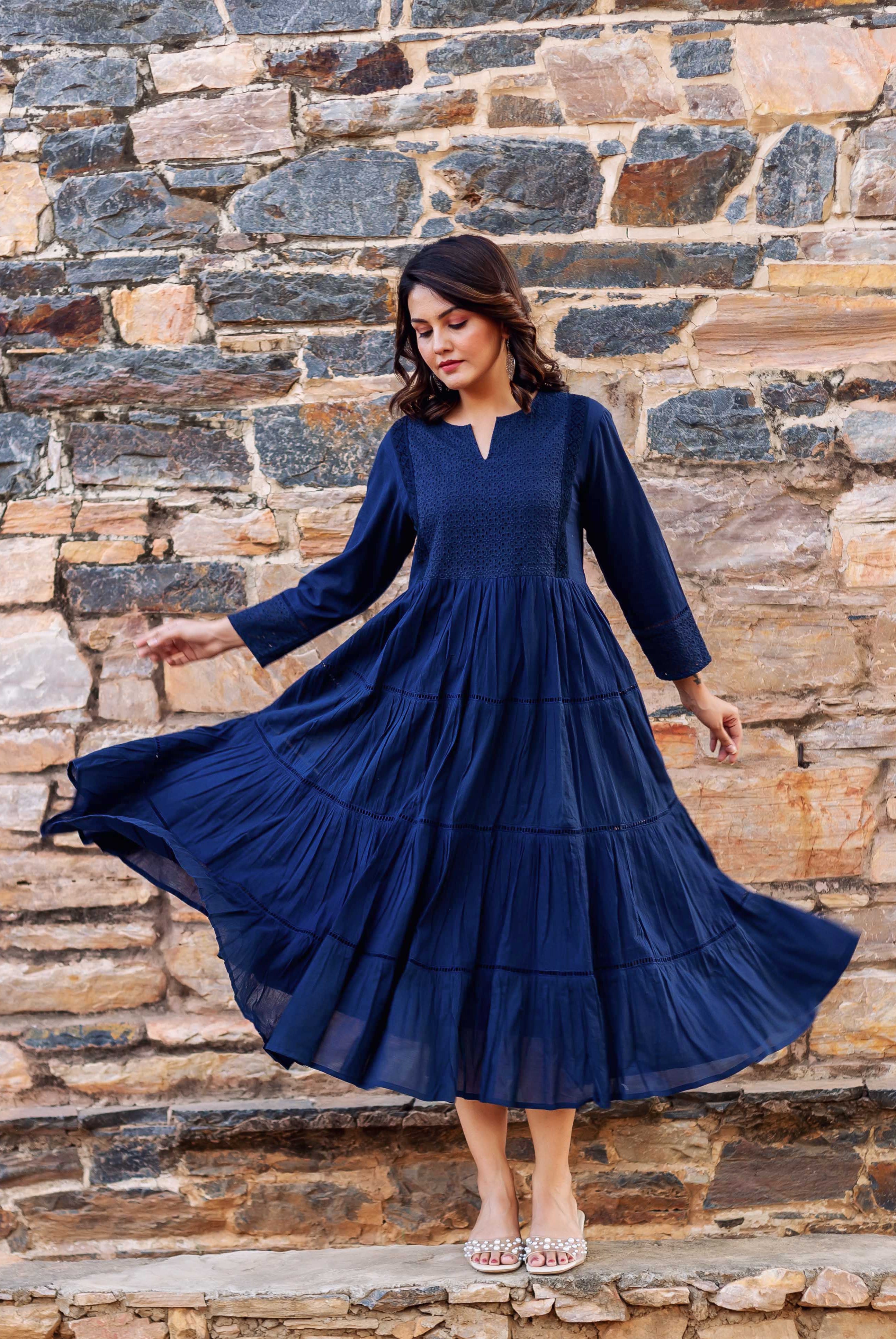 Woman models a flowing indigo tiered dress with delicate embroidery on the bodice.