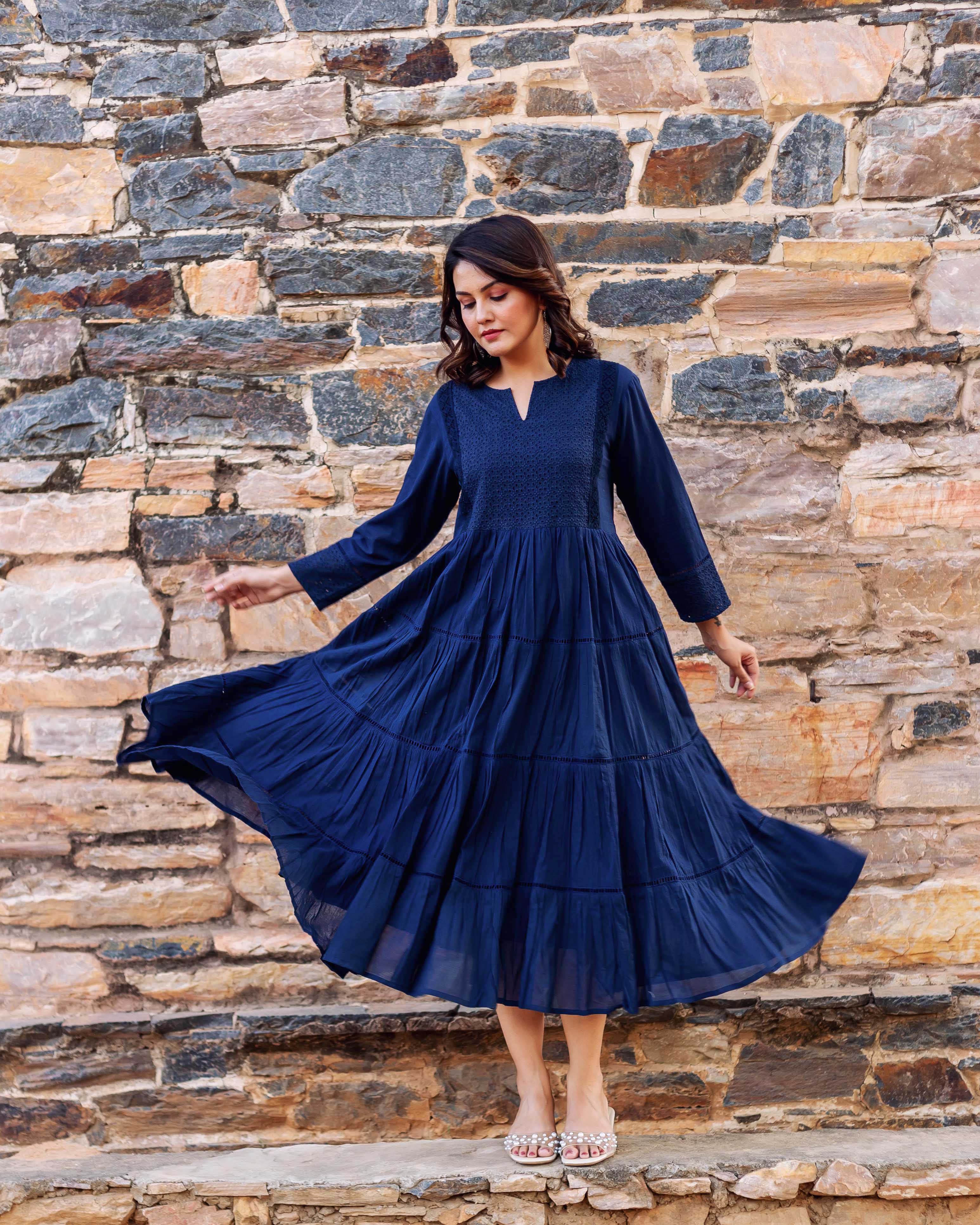 Woman models a flowing indigo tiered dress with delicate embroidery on the bodice.