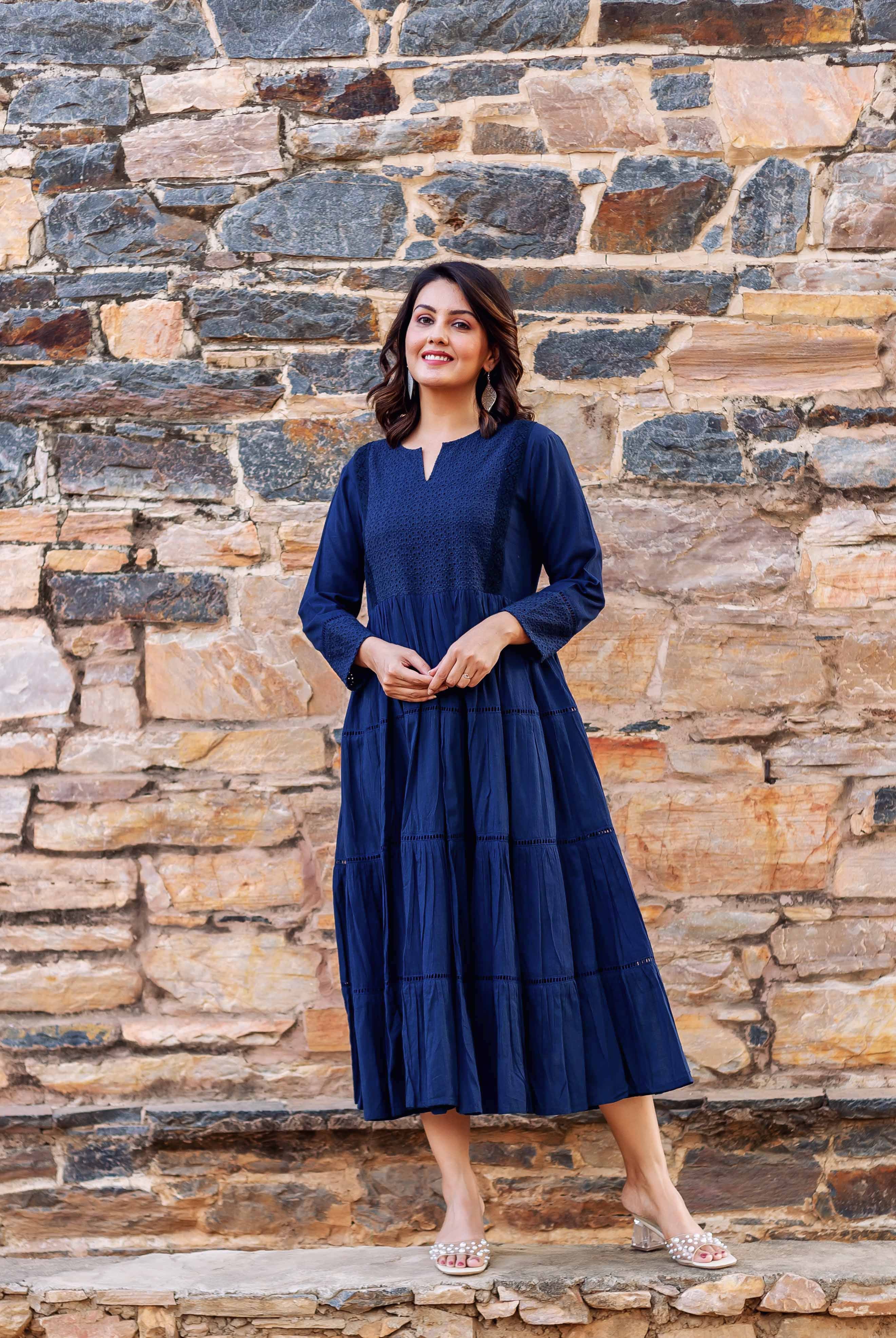 Full-body front view of a model in a deep indigo tiered midi dress with embroidered bodice.