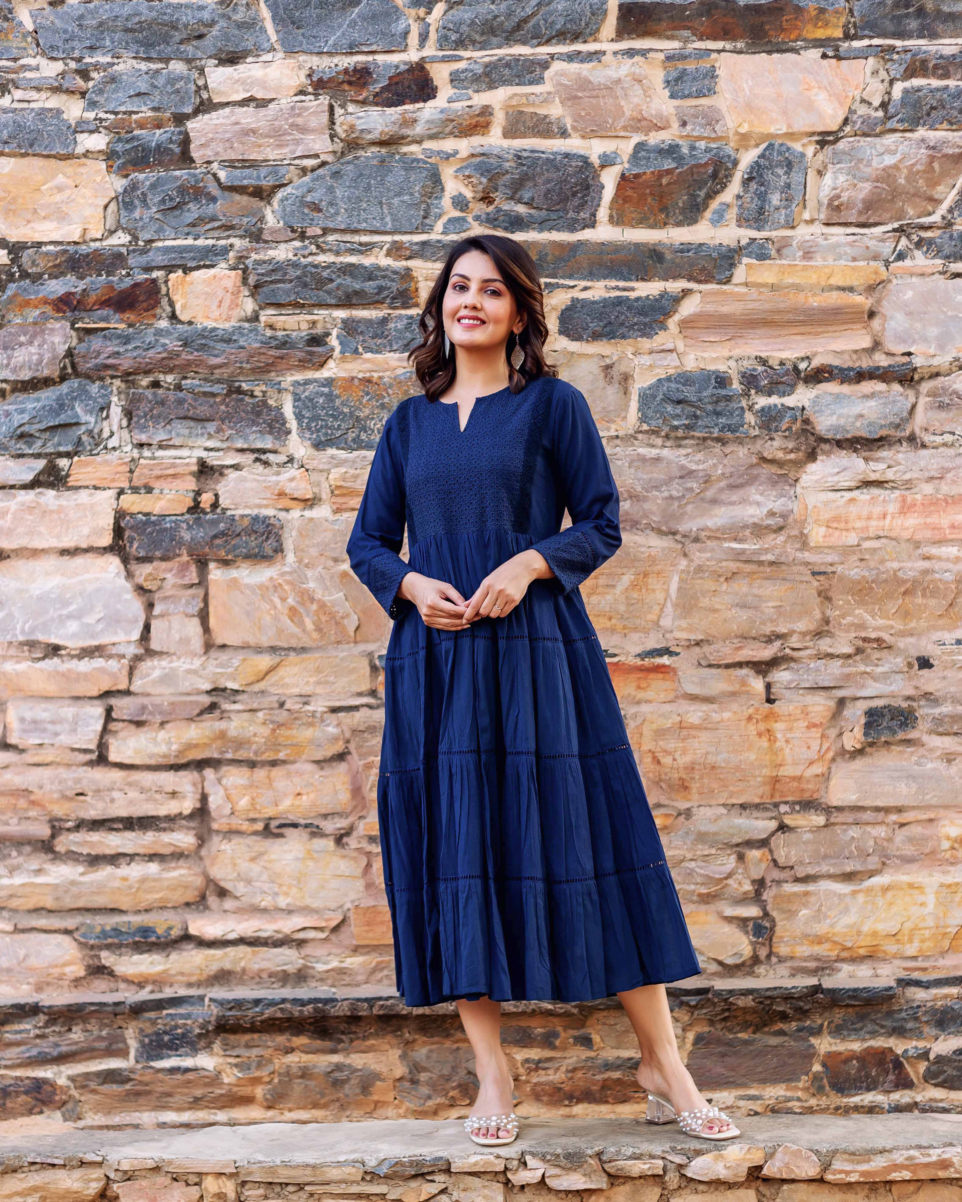 Full-body front view of a model in a deep indigo tiered midi dress with embroidered bodice.