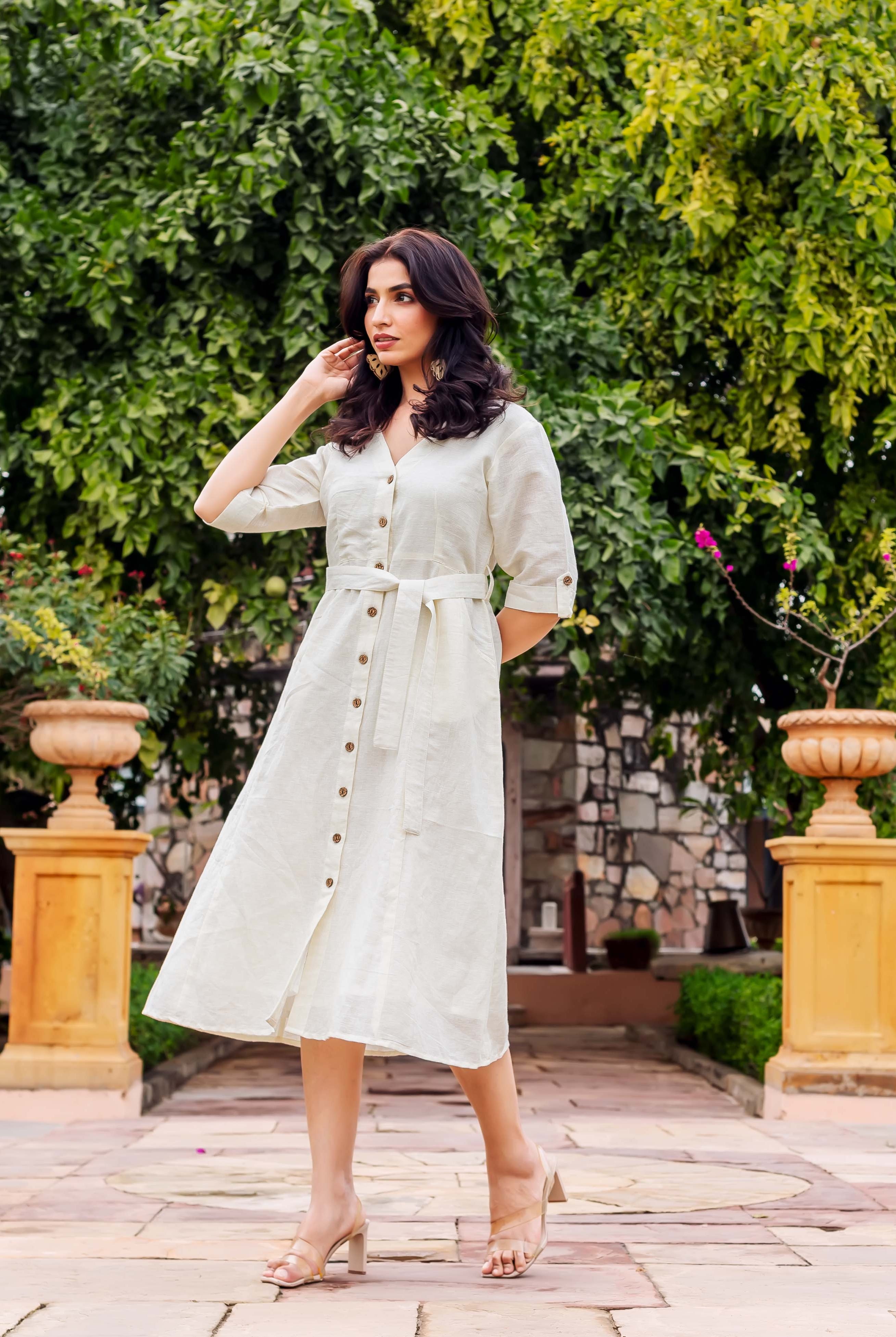 A woman models an off-white button-front belted linen midi dress with 3/4 sleeves.