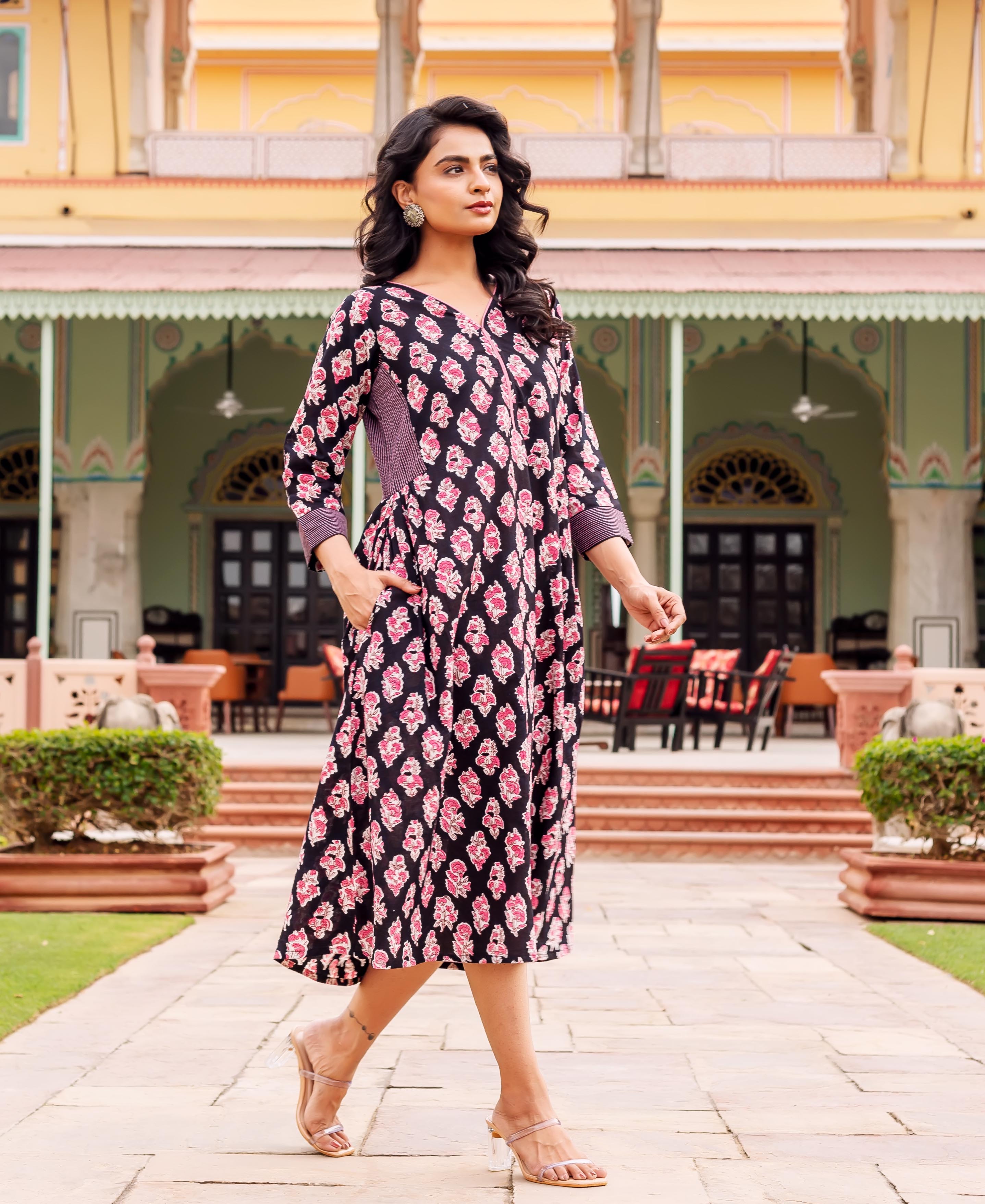 A woman in a black, pink, and white floral dress with a V-neckline and 3/4 sleeves.