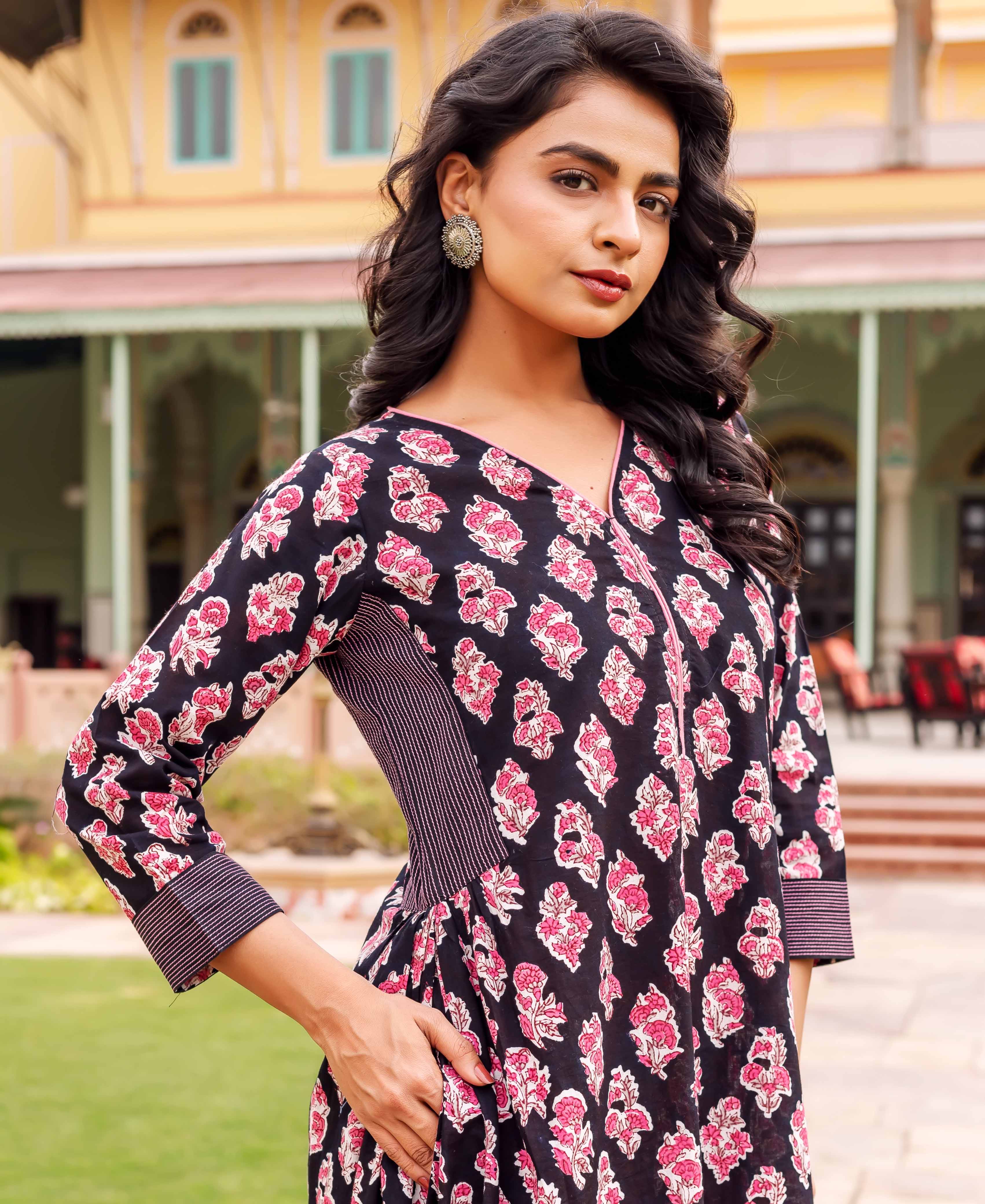 A woman wearing a black dress with pink floral print and striped accents.
