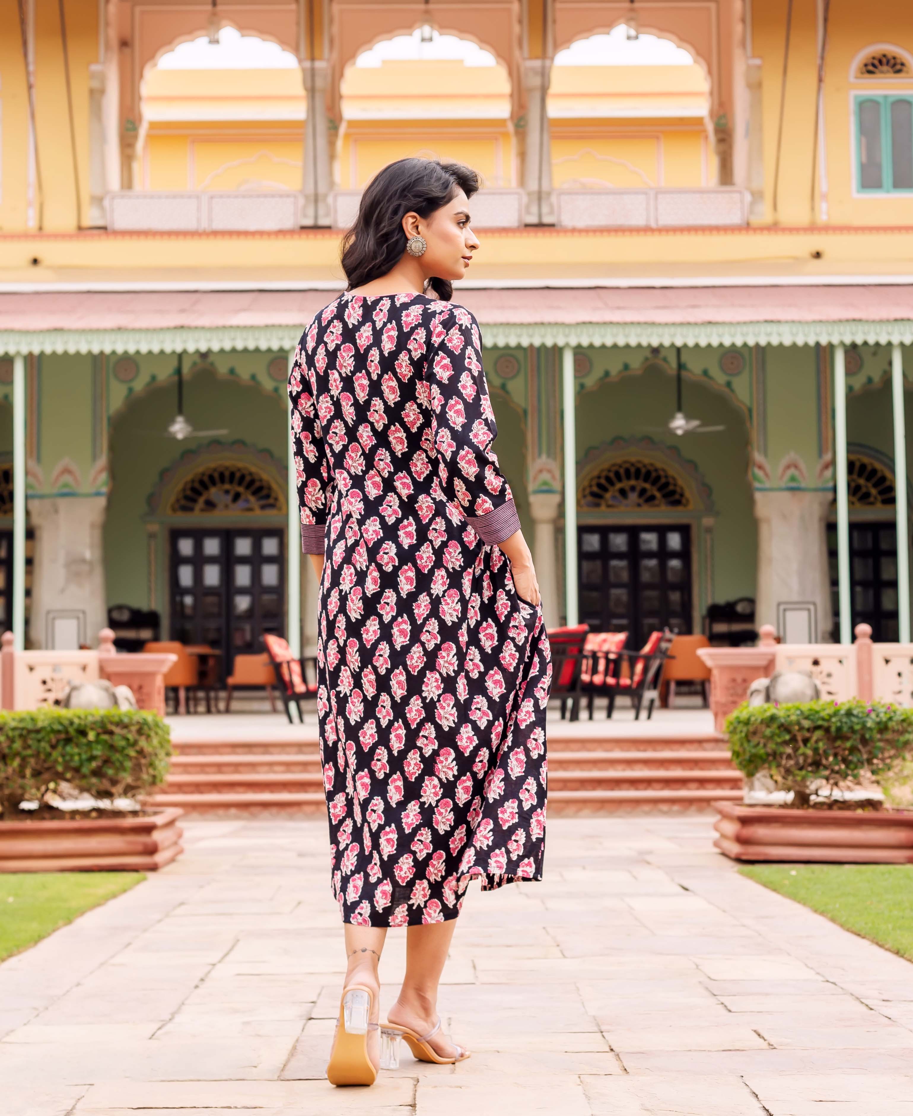 A woman in a black dress with pink floral print, standing in front of a building.