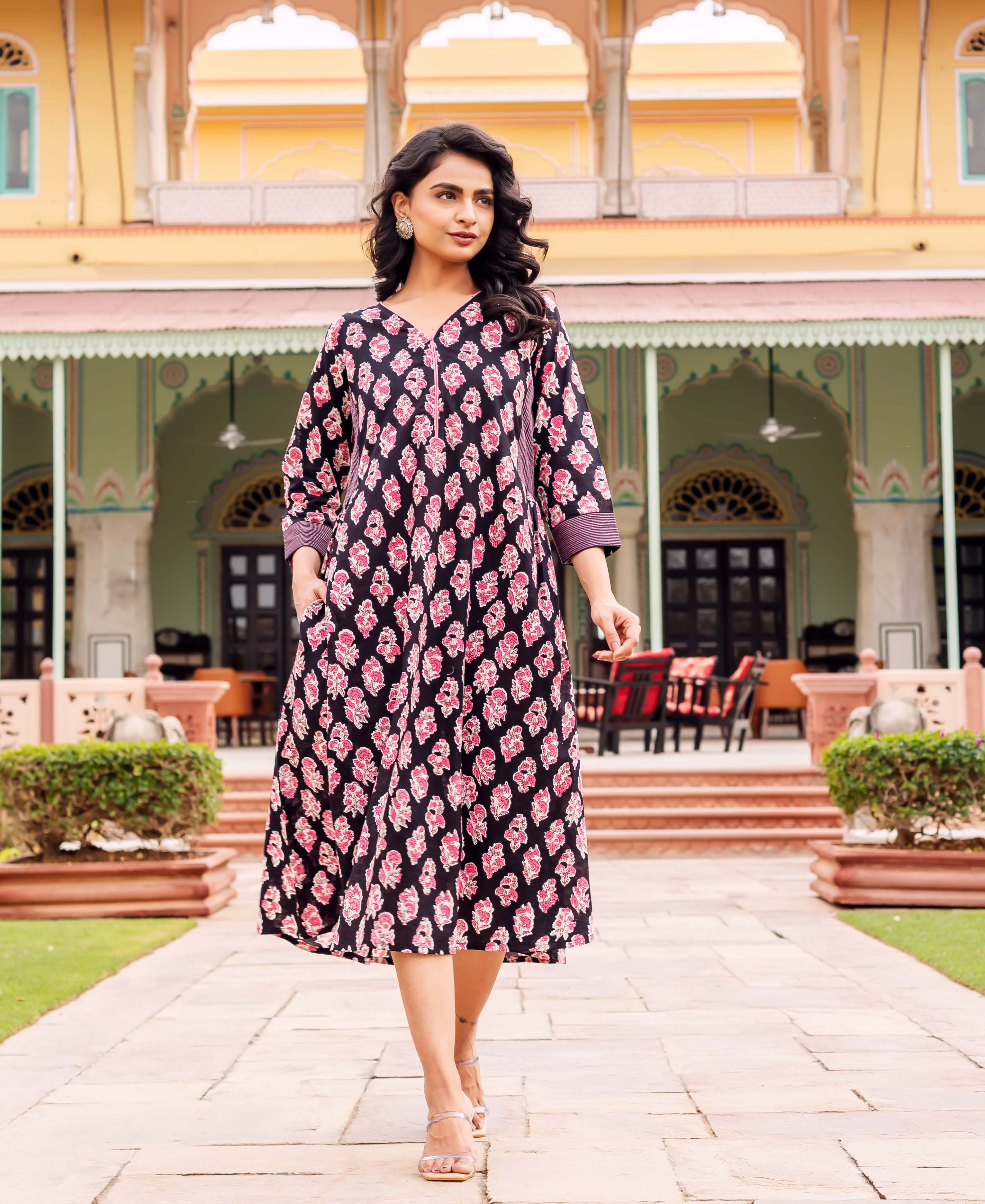 A woman in a black, pink, and white floral dress walks on a stone path.