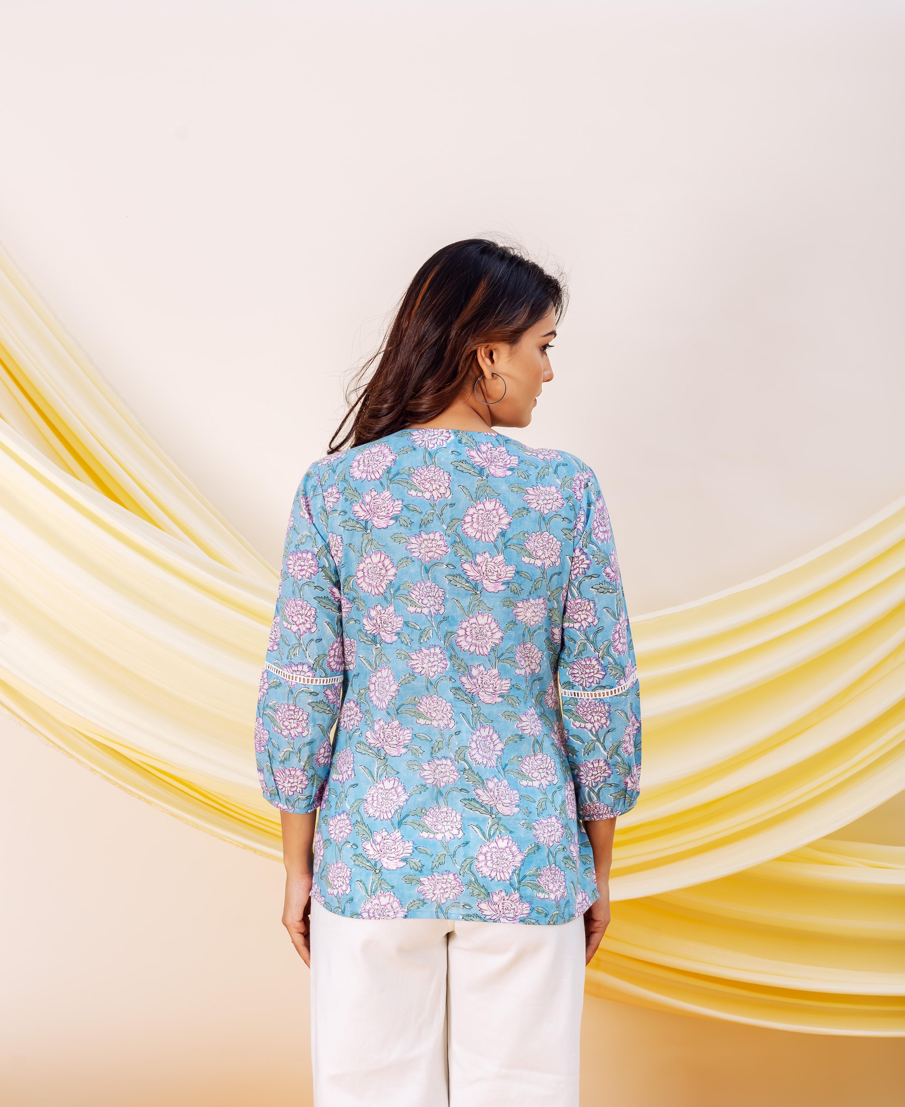 Woman's back in blue floral top with pink flowers and white pants against yellow drapes.