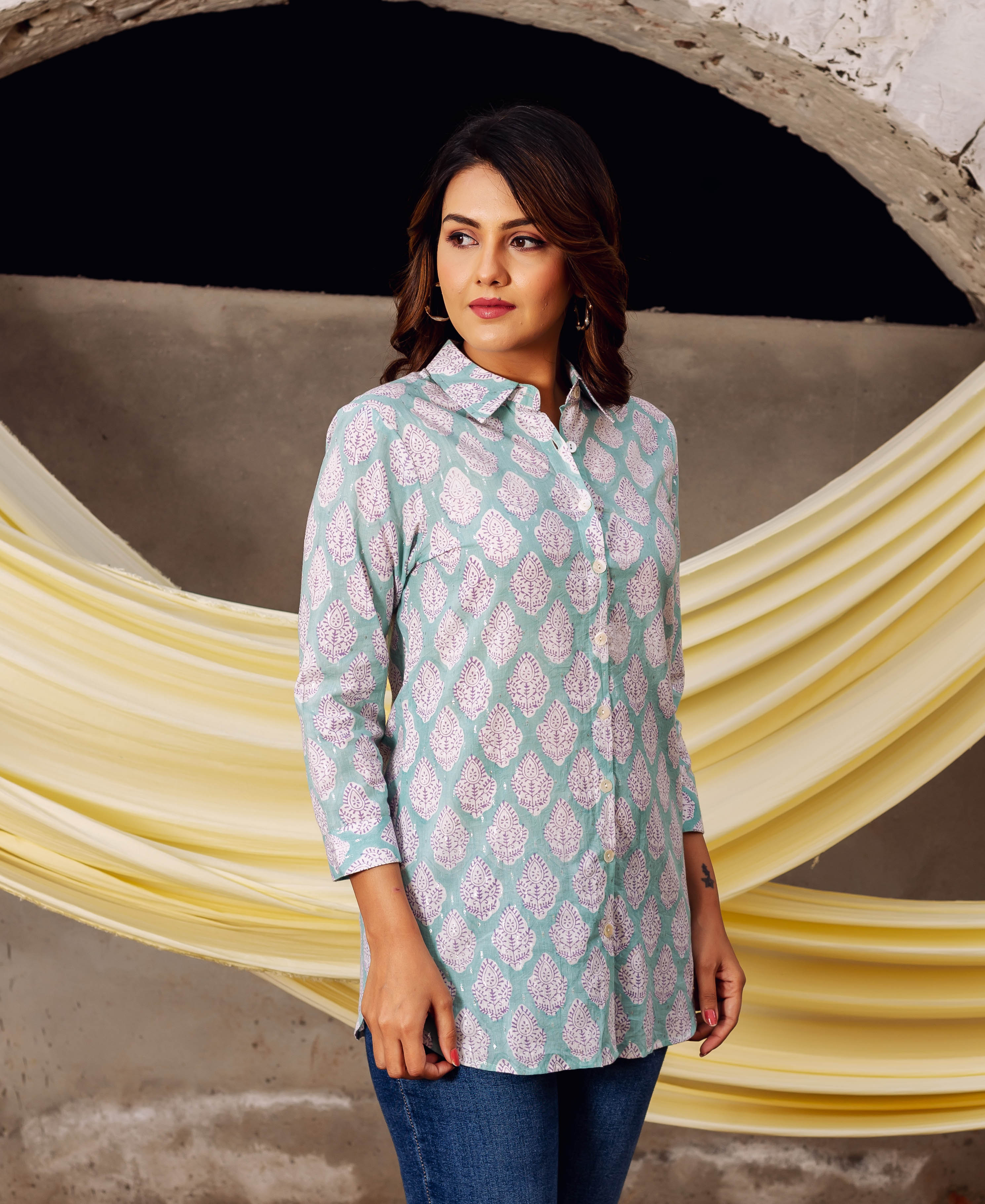 Woman in a light teal block printed collared shirt with white leaf patterns.