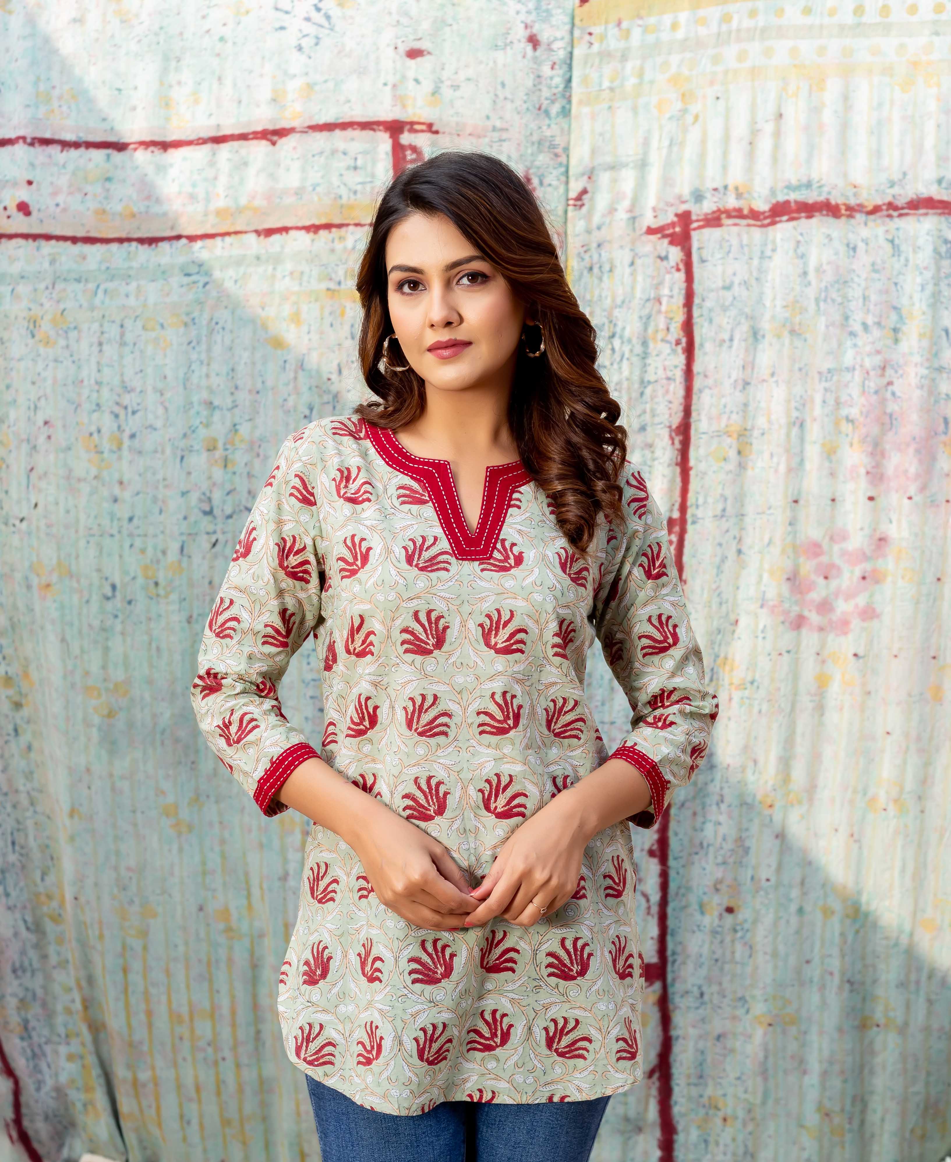 Front-facing model wearing a meadow green block-printed top with red V-neck and leafy pattern.