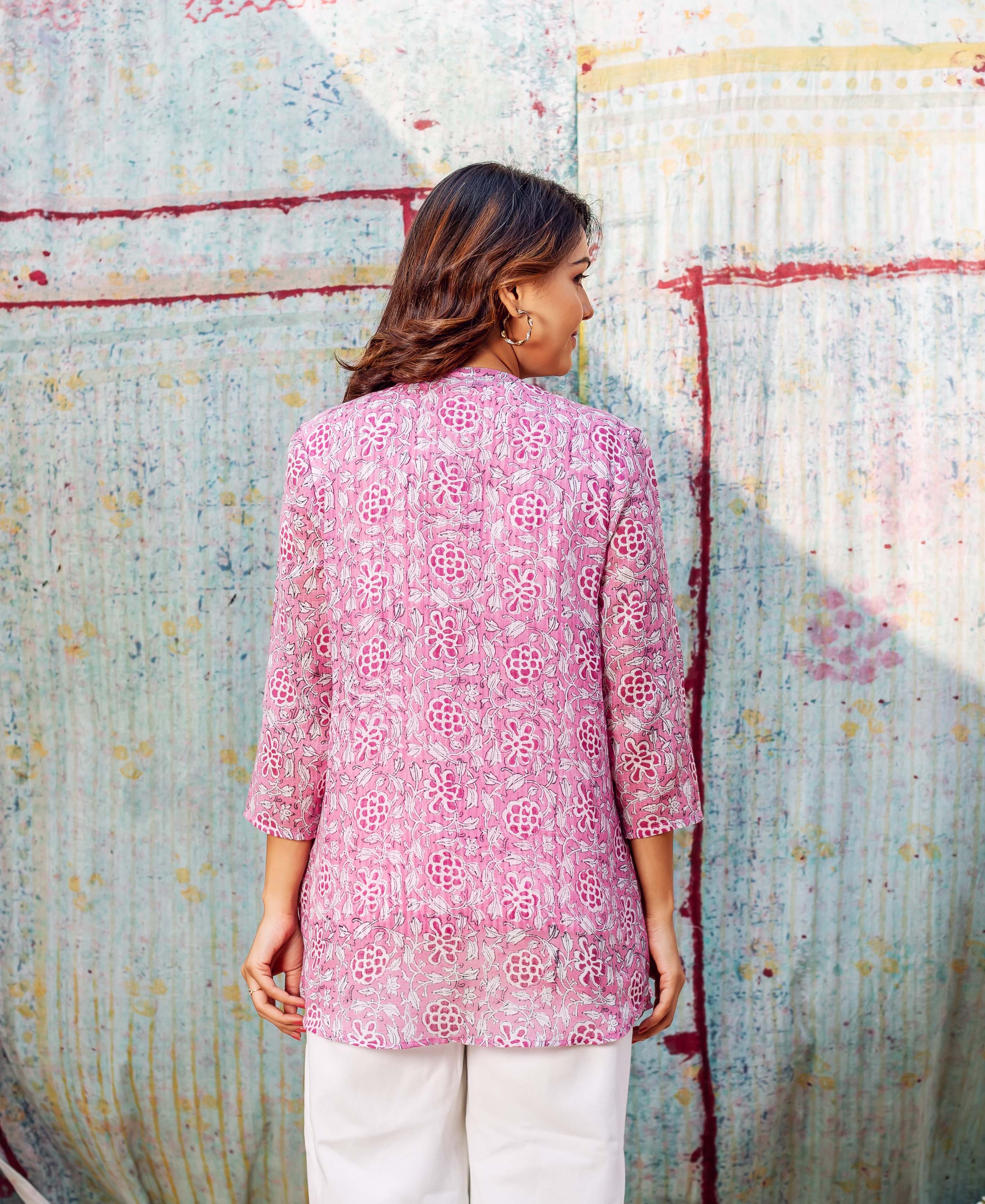 A model wearing a pink floral top with white pants, facing away from the camera.