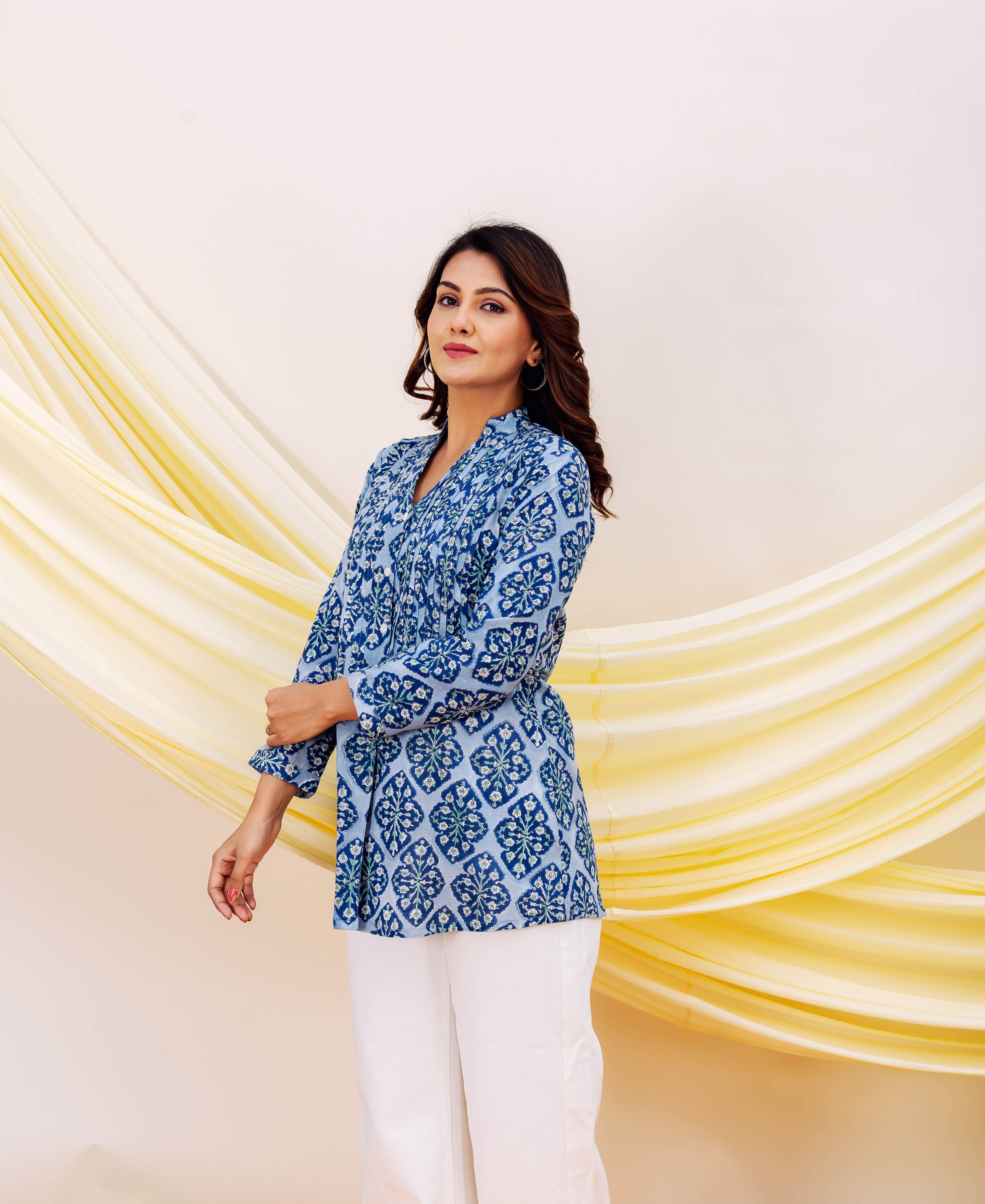 Three-quarter shot of a woman wearing a blue hand-printed tunic with ethnic patterns and white pants.