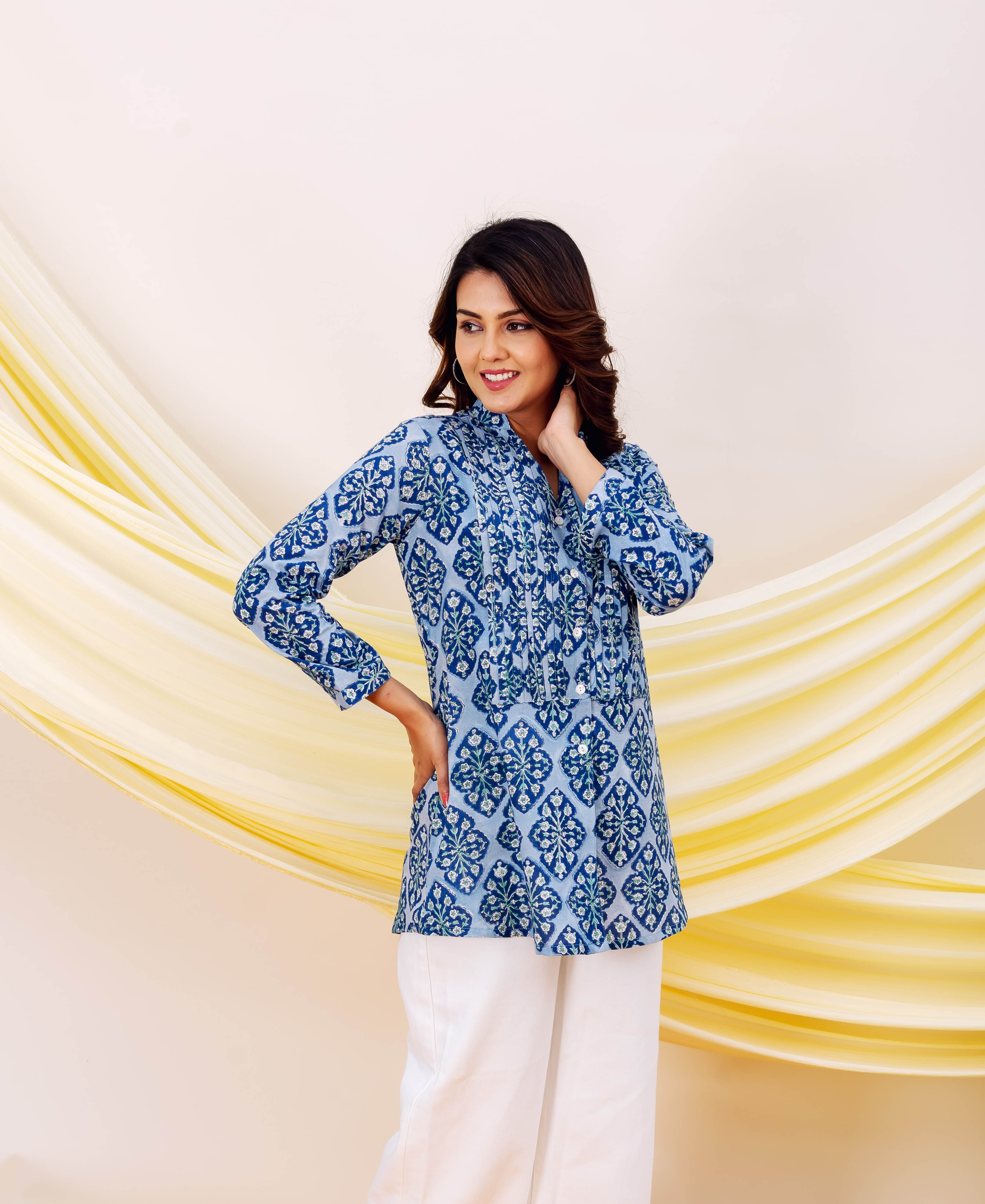 Standing model in a blue hand-block printed floral-geometric tunic top with white trousers.