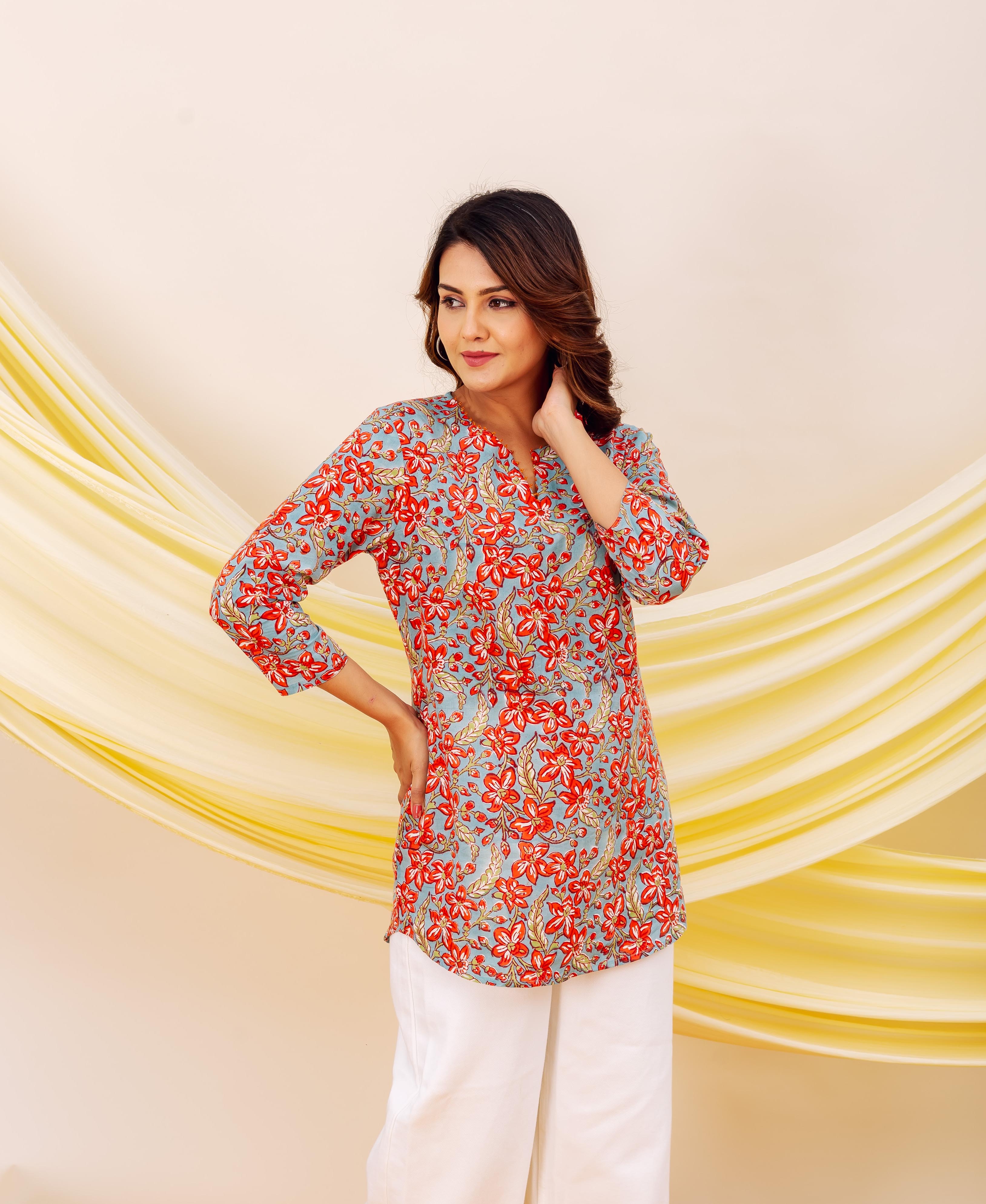 Front view of model in light blue top with vibrant red floral print and white pants.