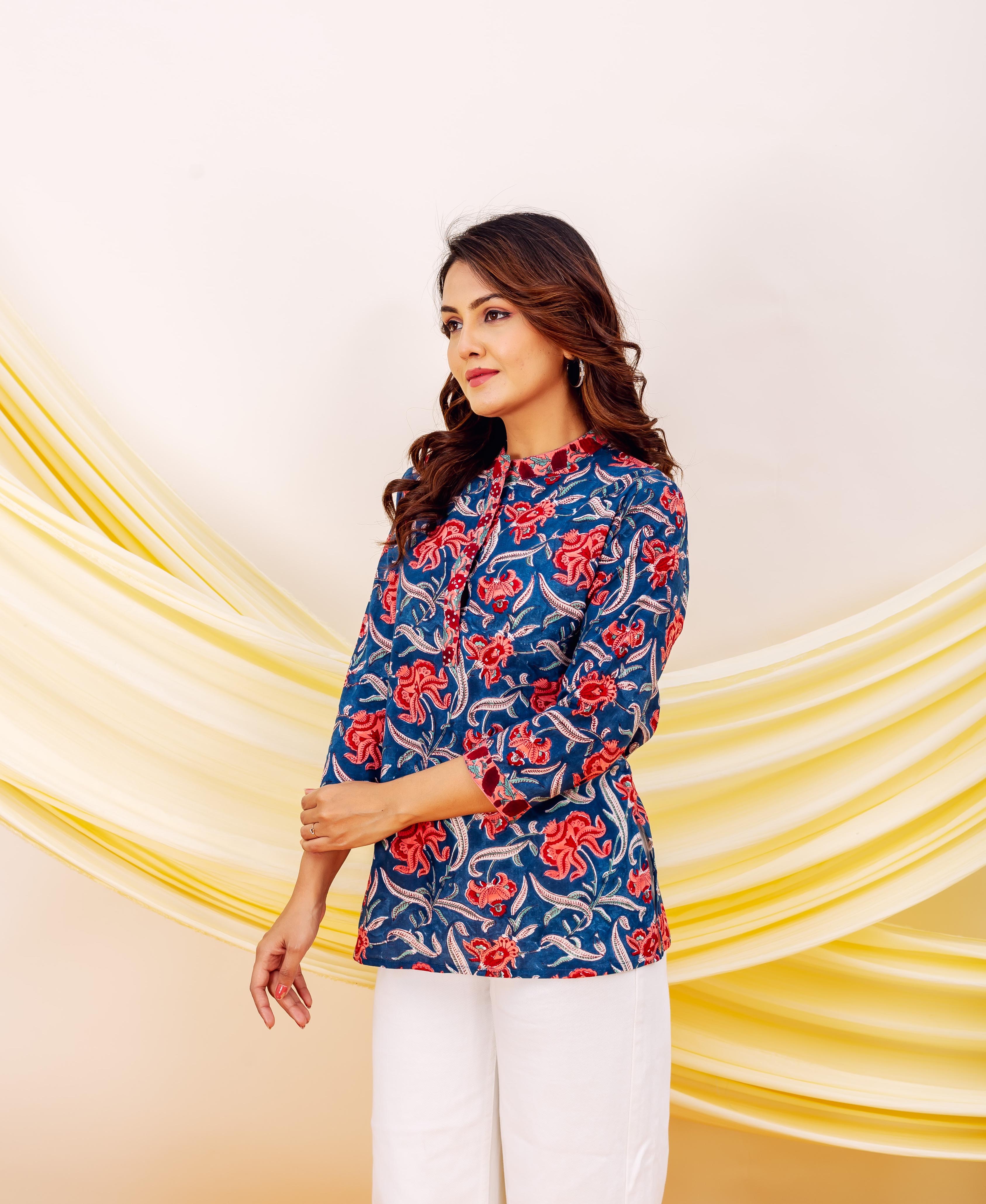 Woman wears blue hand-block-printed top with scarlet red floral print, paired with white pants.