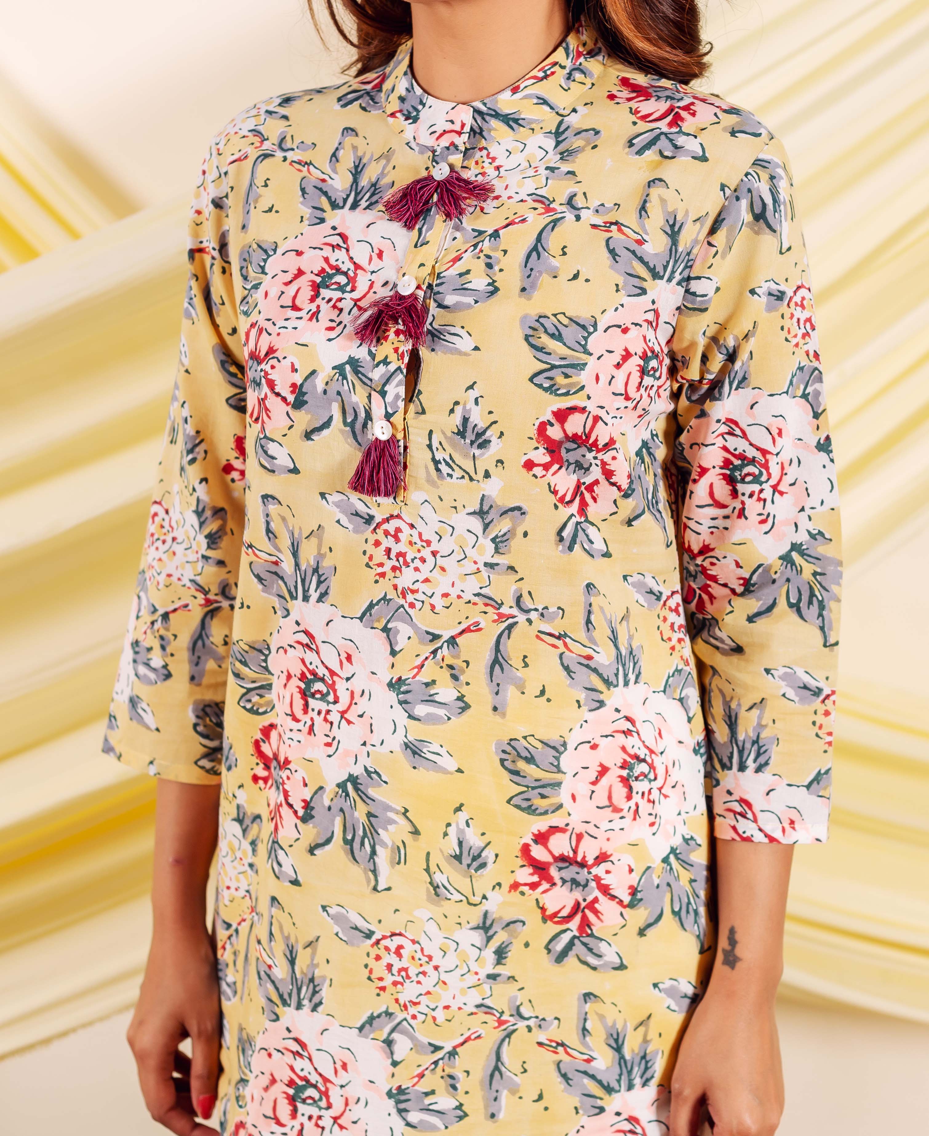 Front view of woman wearing yellow floral hand-block-printed tunic with burgundy tassels.