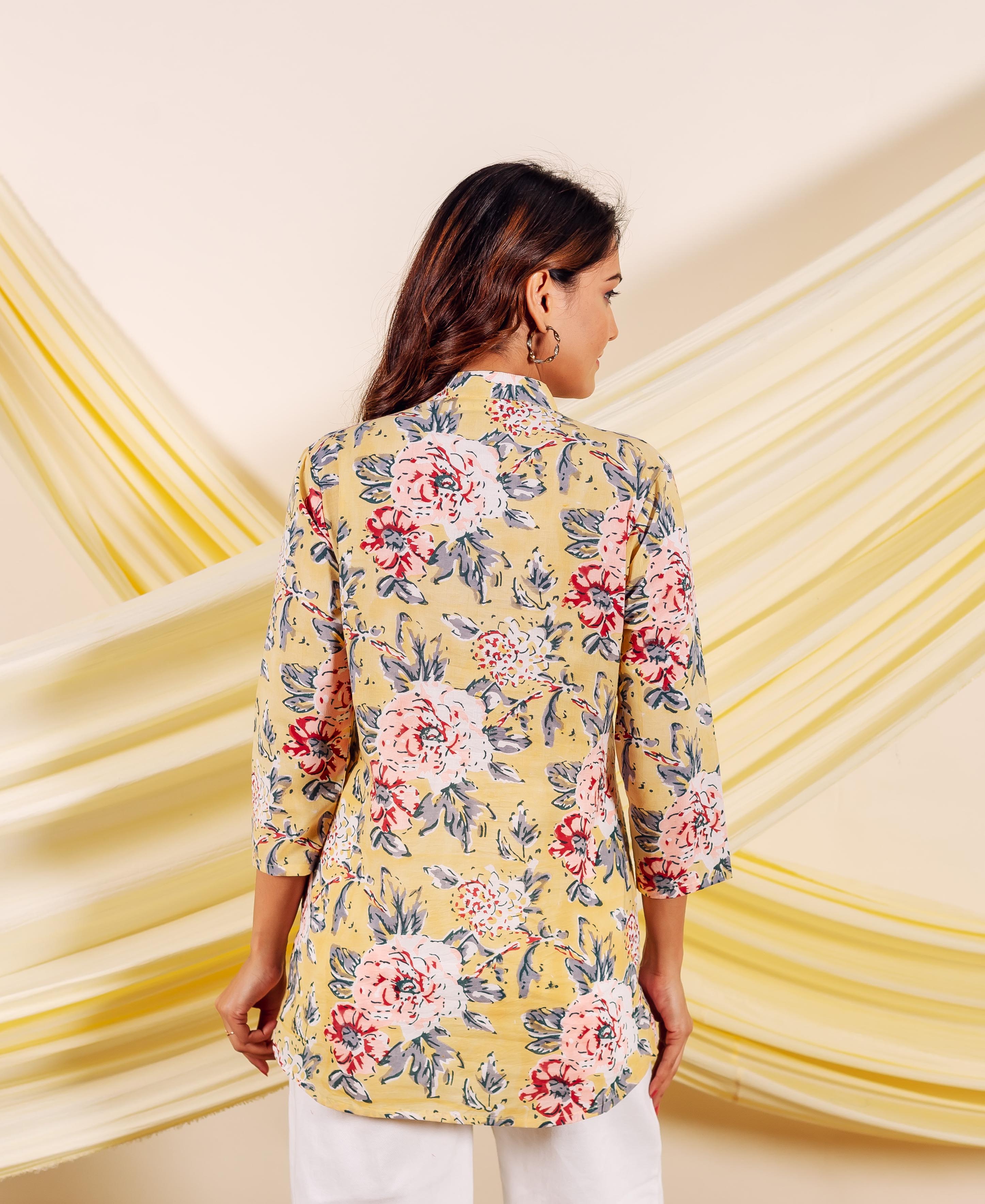 Back view of model wearing a yellow floral top with red and grey blossoms.