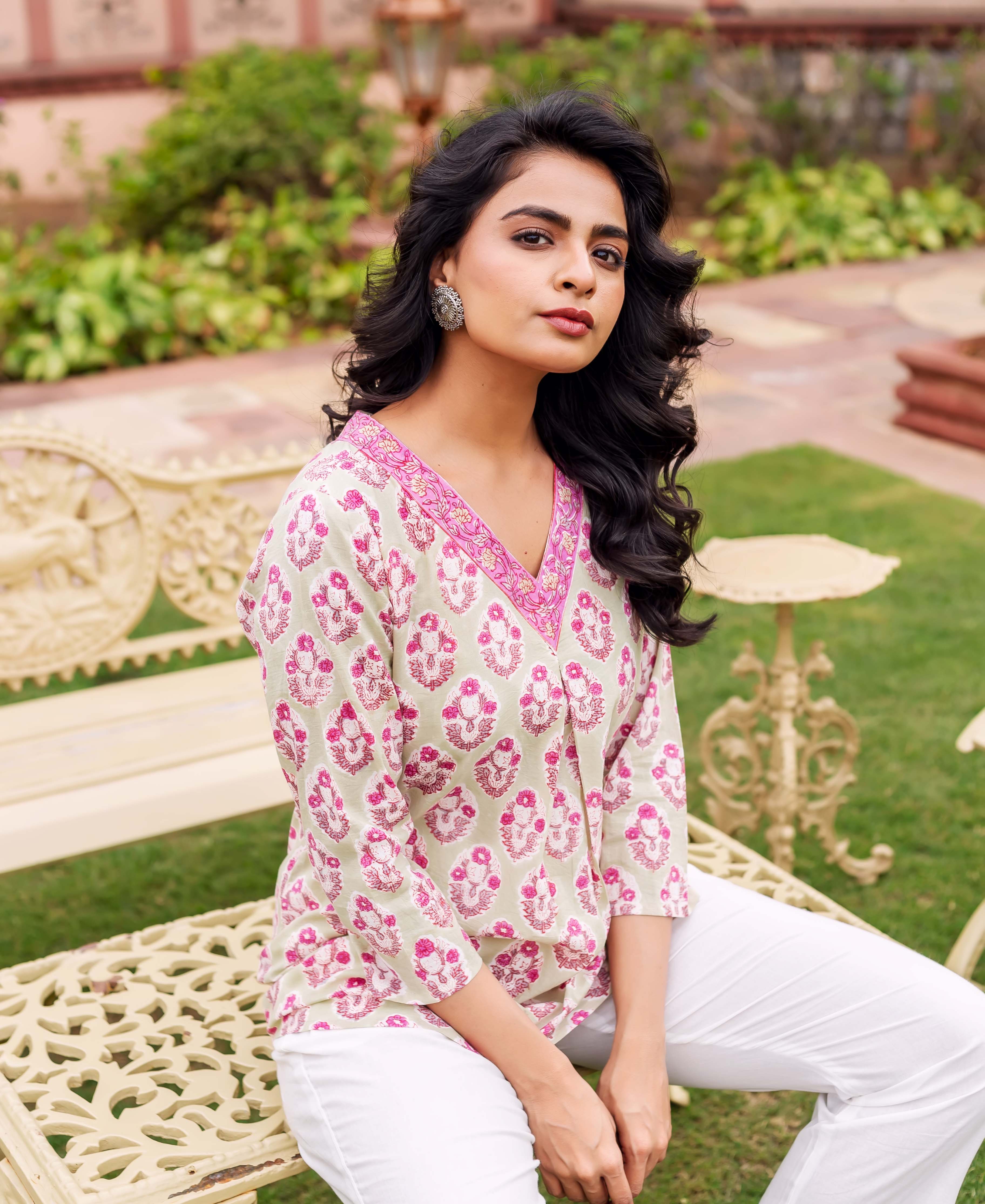 A woman sitting on a bench, wearing a mint green tunic with pink floral print.