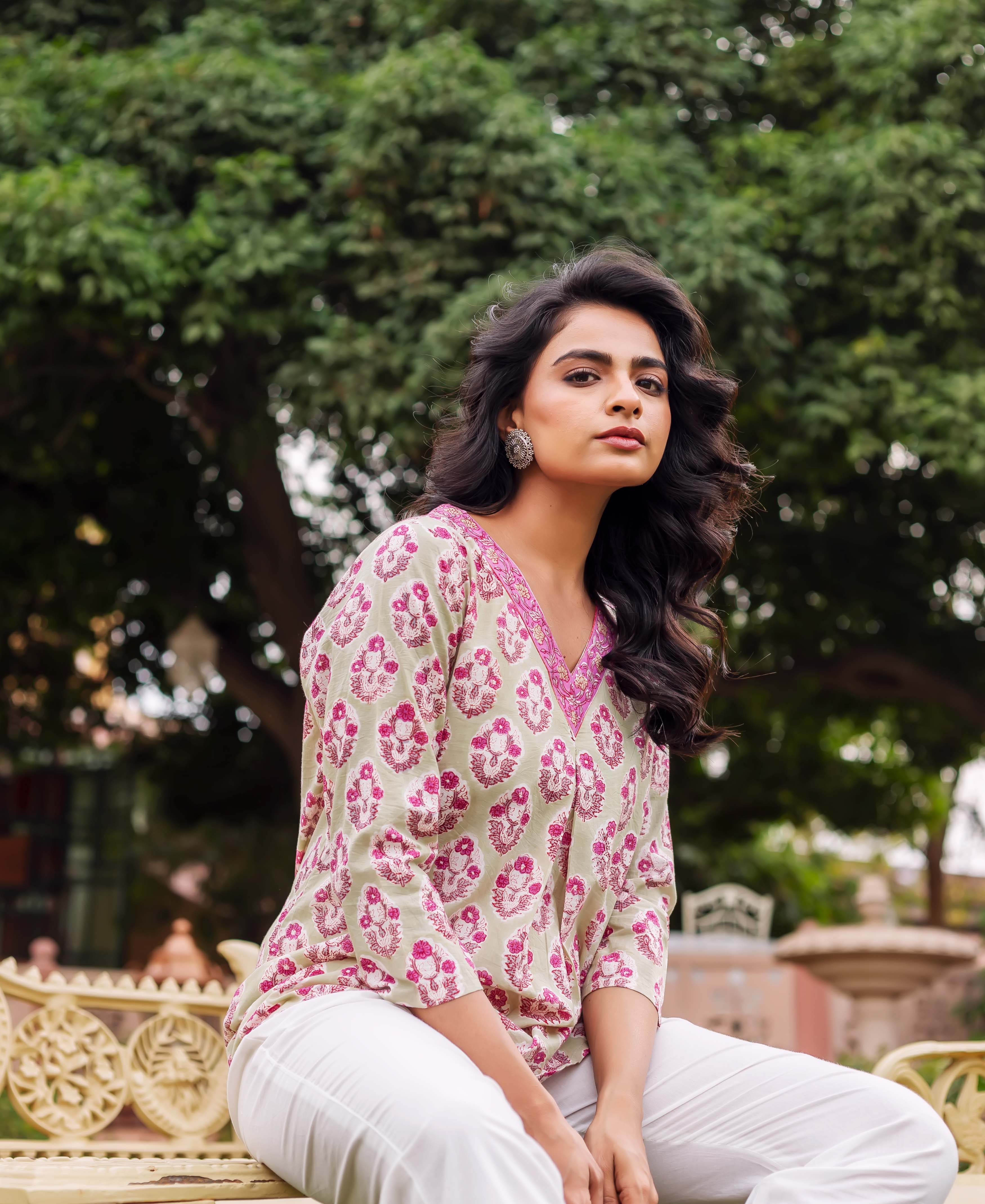 Woman sitting on a bench wearing a mint green tunic with pink floral print.