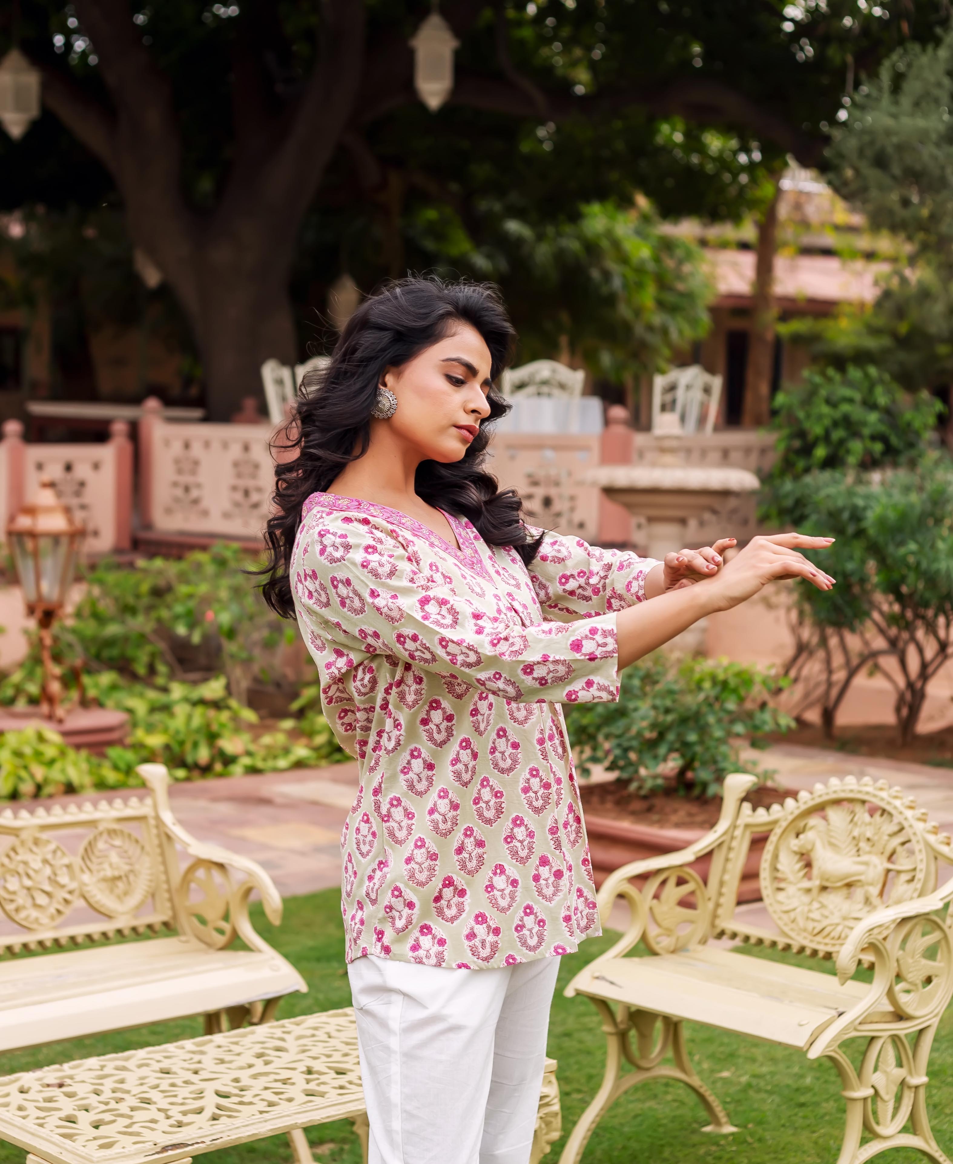 A model wearing a mint green tunic with pink block print, standing in a garden.