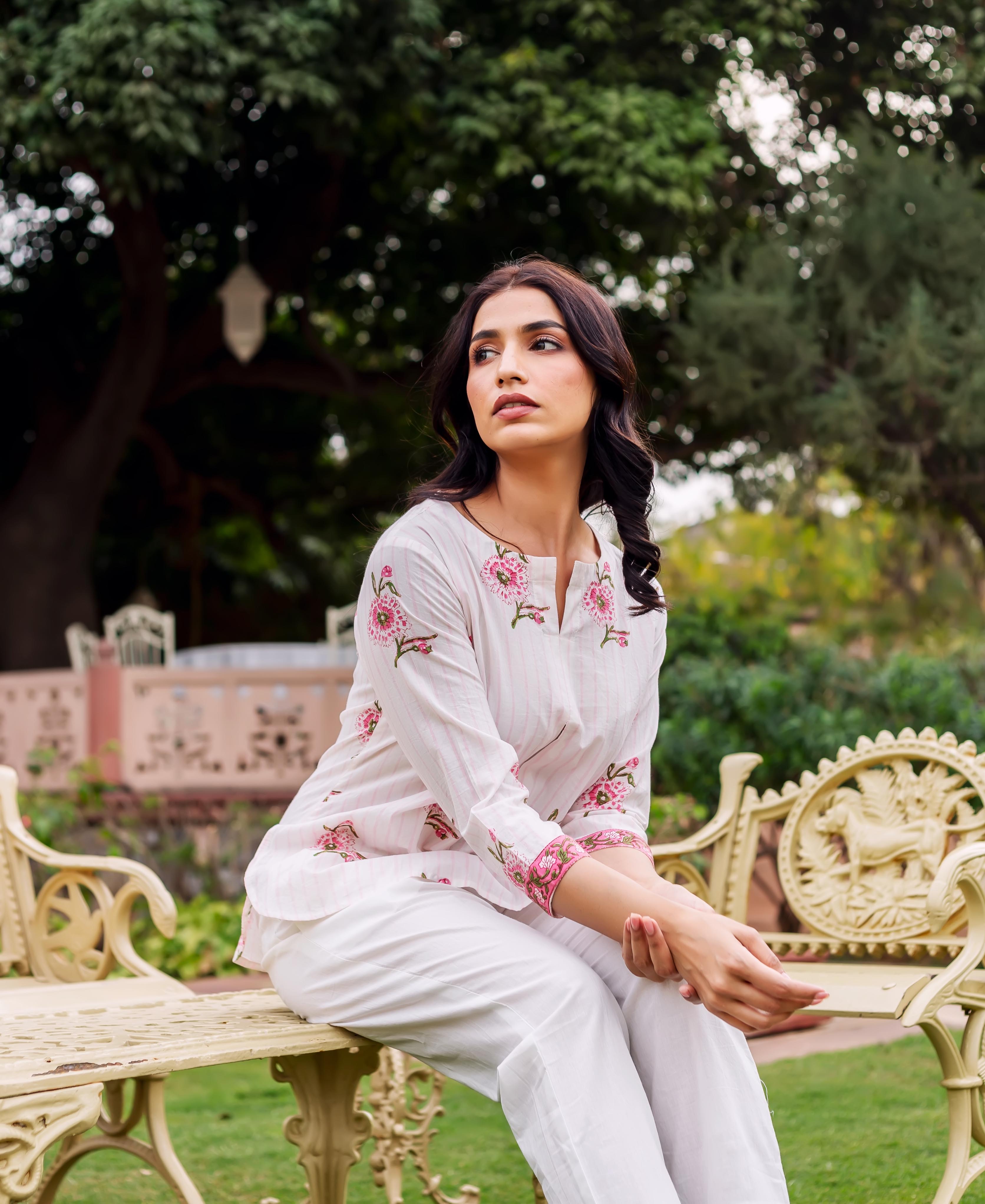 Woman wearing white block-printed tunic with pink floral motifs and matching white pants.