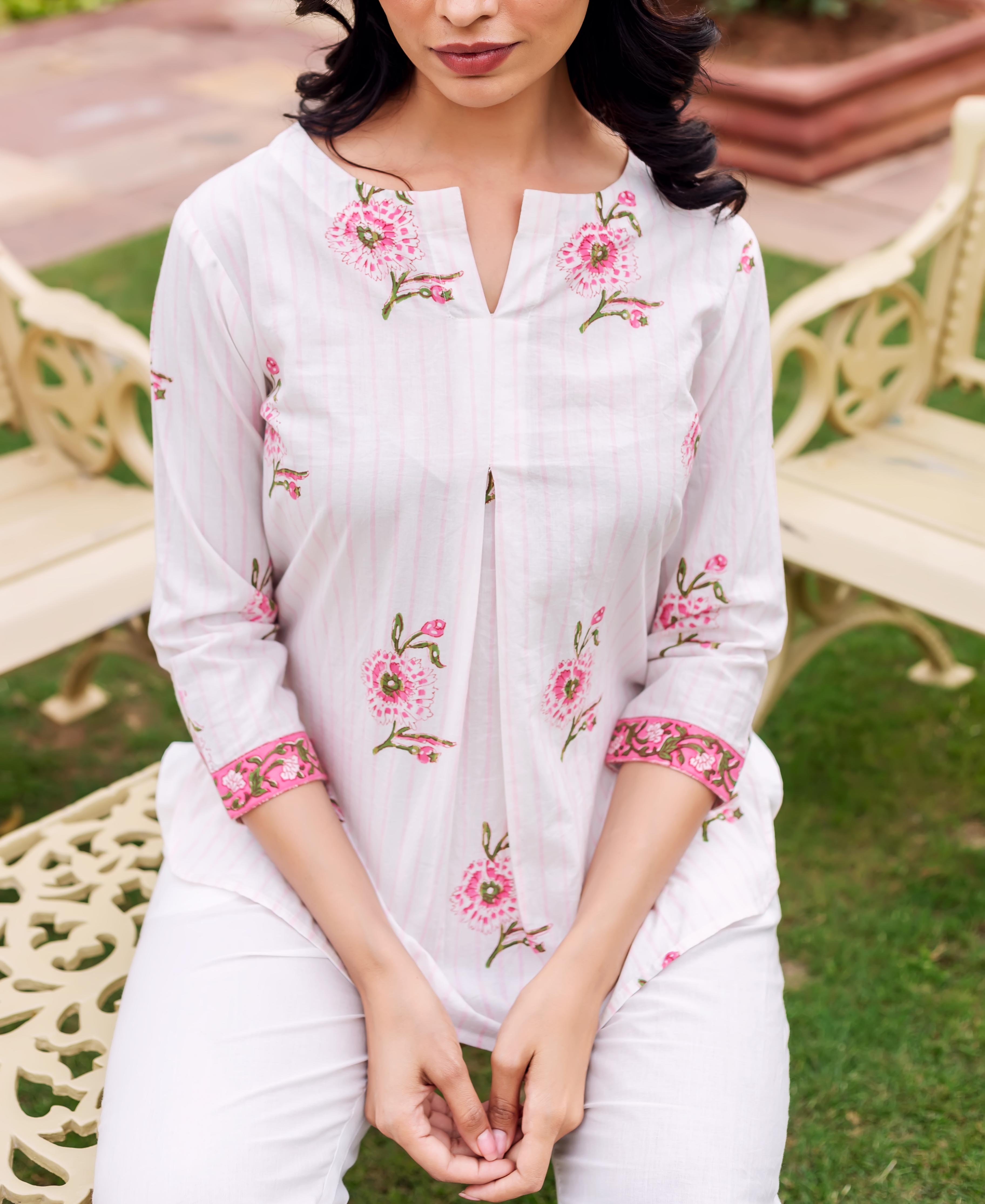 White tunic with pink stripes and floral embroidery, on a woman sitting outdoors.