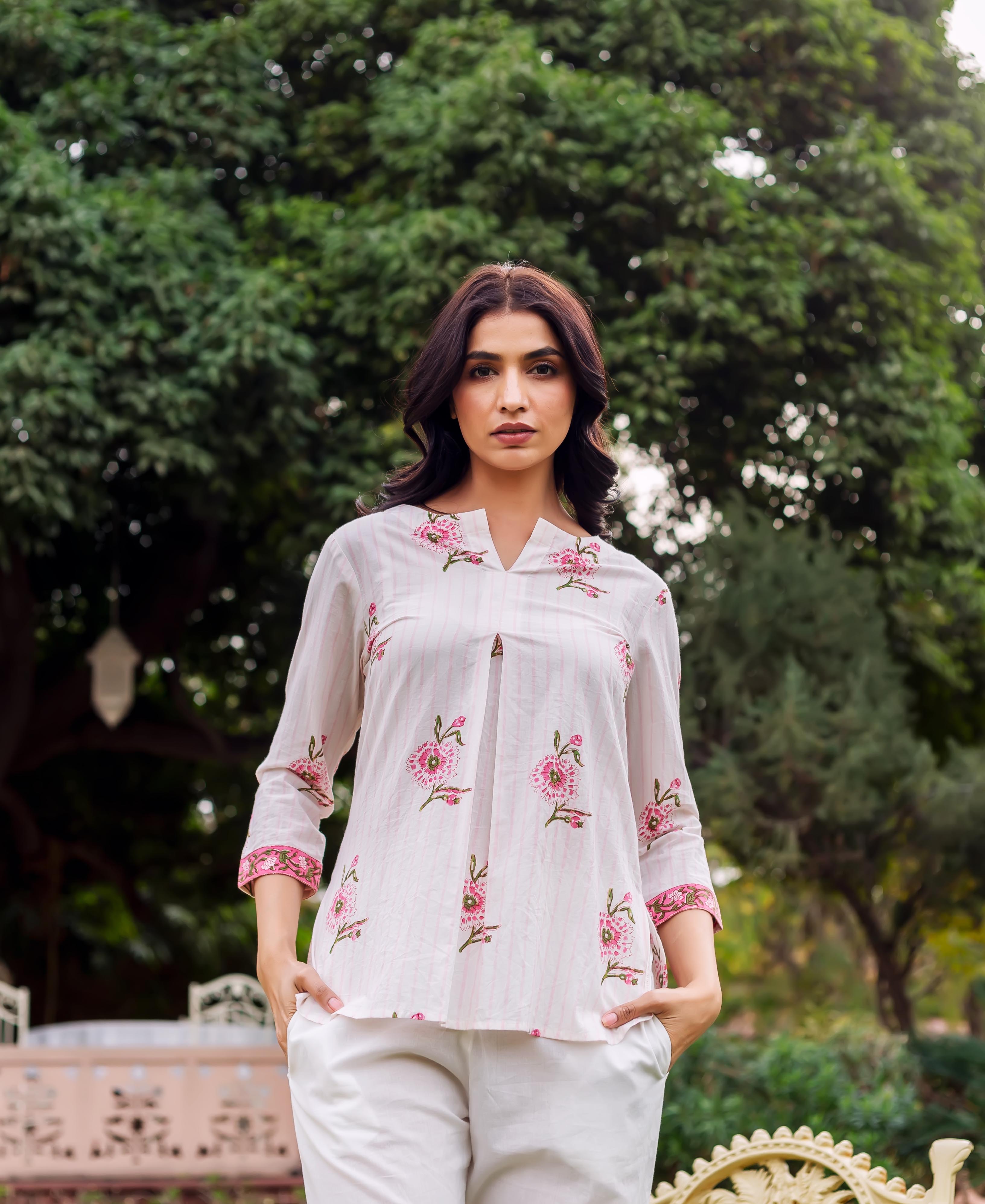 Model wears a white block-printed tunic with pink flowers, stripes, and white pants.